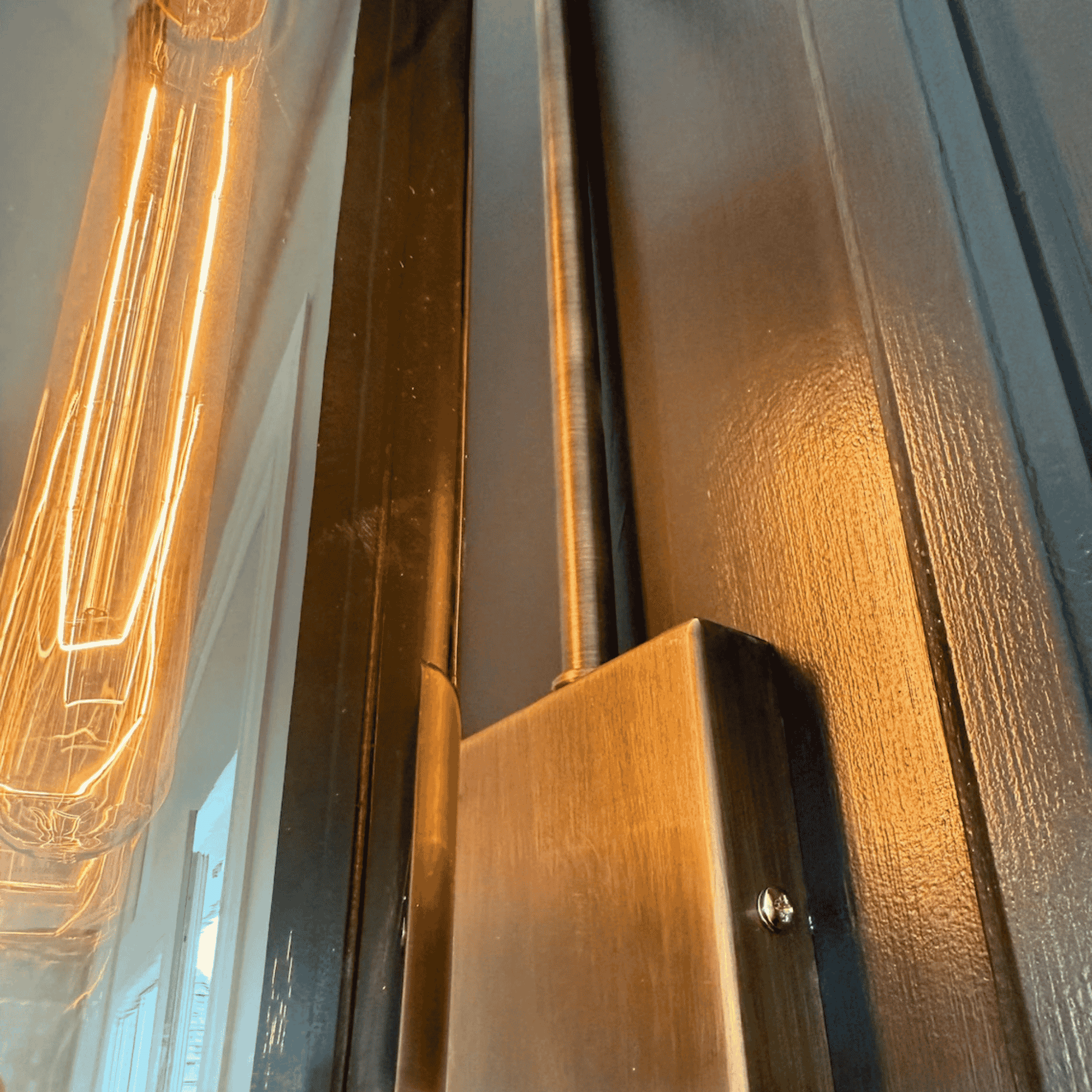Close-up of blown glass wall sconce showing antique hardware and glowing filament bulb.