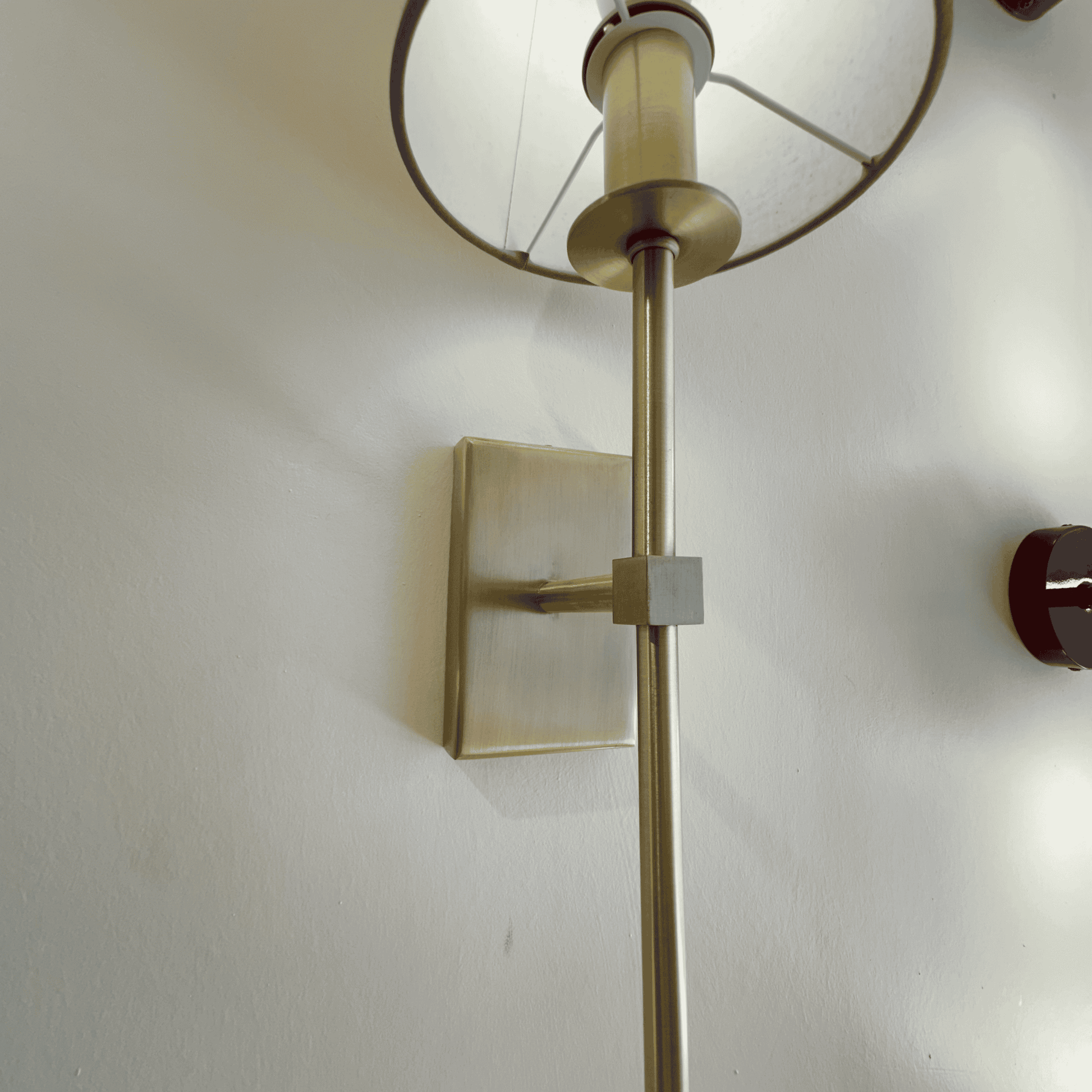 Close-up view of a brass wall sconce showing modern fixture details and fabric shade frame against a white wall.
