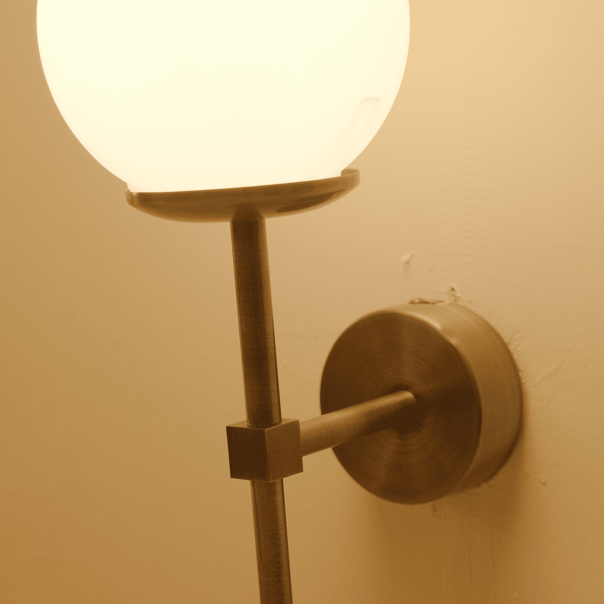 Close-up of a brass wall sconce showcasing the frosted globe shade and mounting hardware.