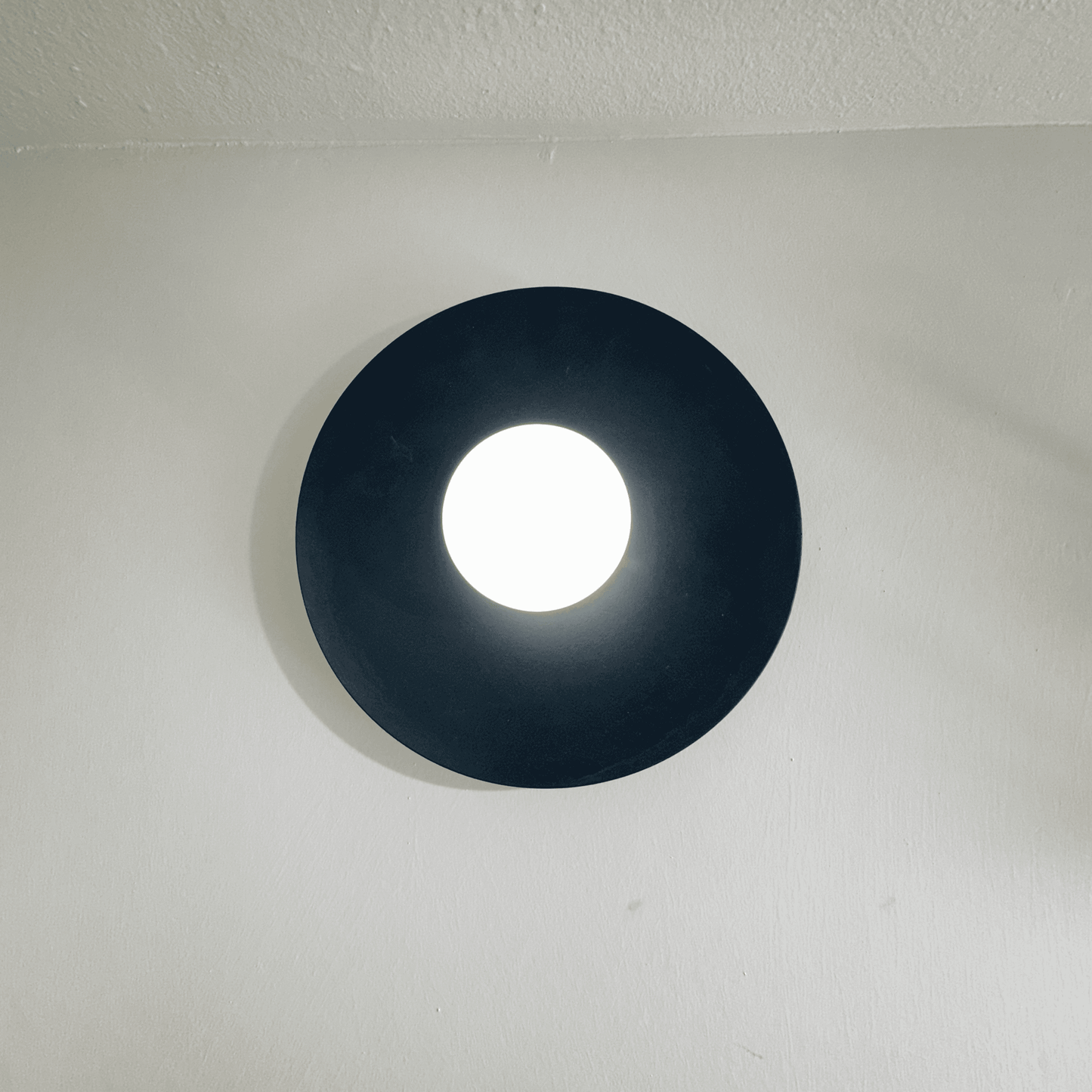 Contemporary black disc wall sconce with diffused white glow in a modern wall setting.