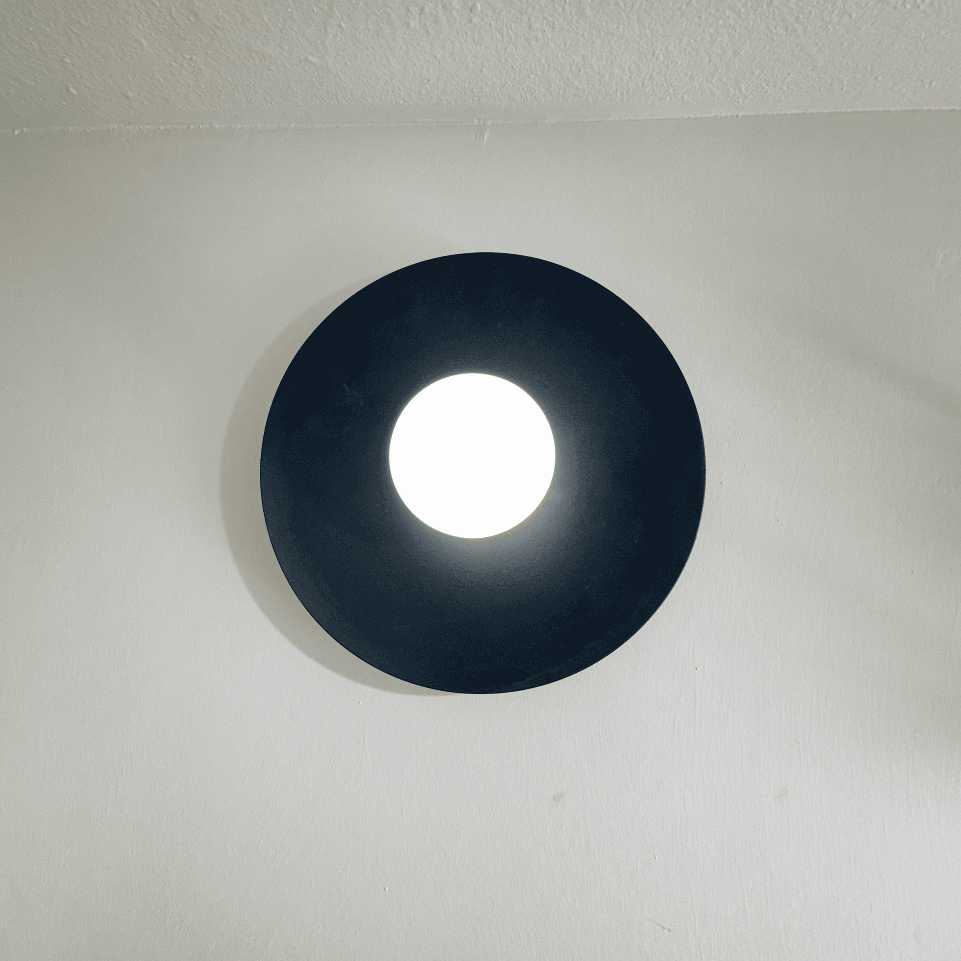 Contemporary black disc wall sconce with diffused white glow in a modern wall setting.