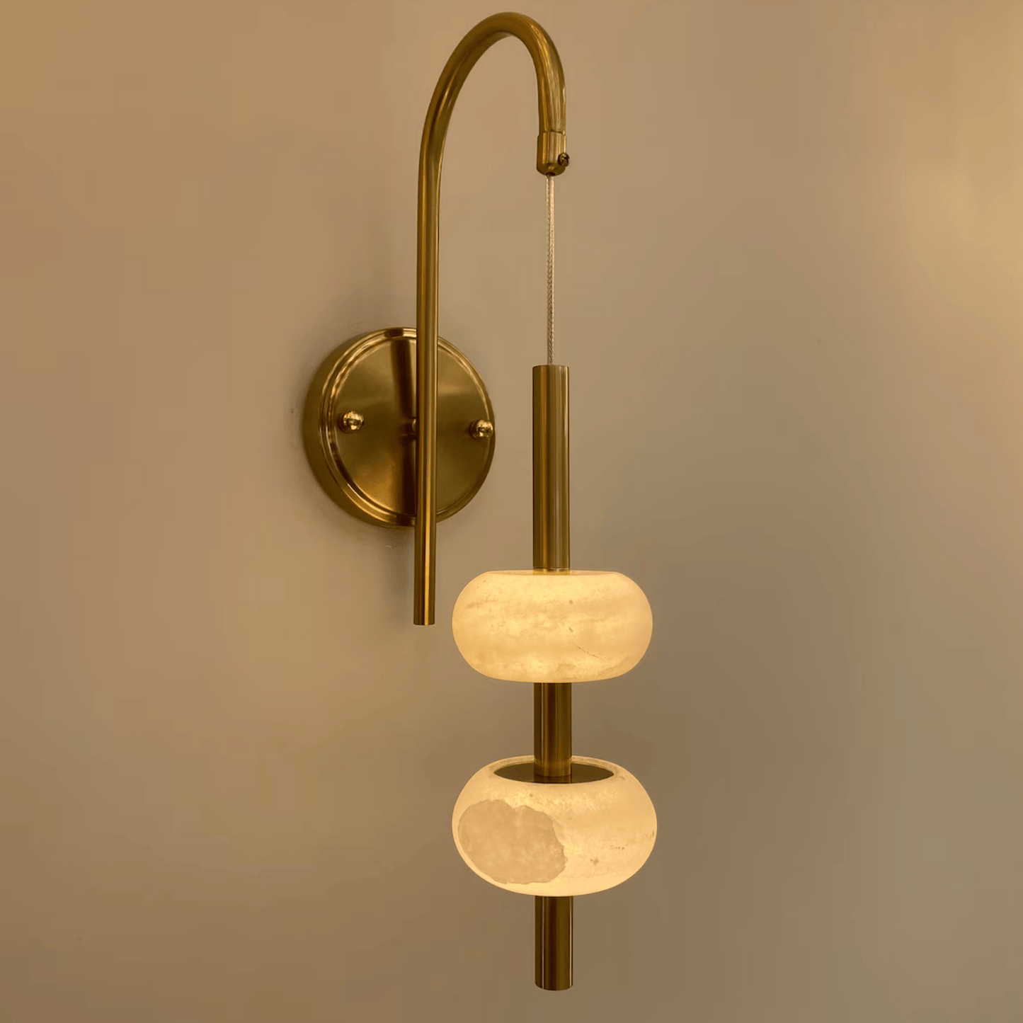 Contemporary brass wall sconce with glowing alabaster shades mounted on a curved arm.