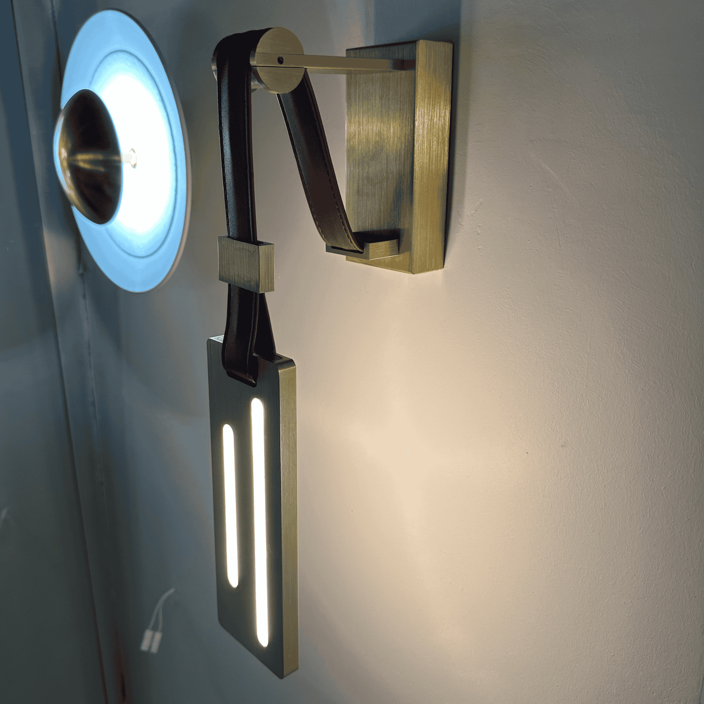 Contemporary wall-mounted leather sconce with brass arm and vertical LED lighting.