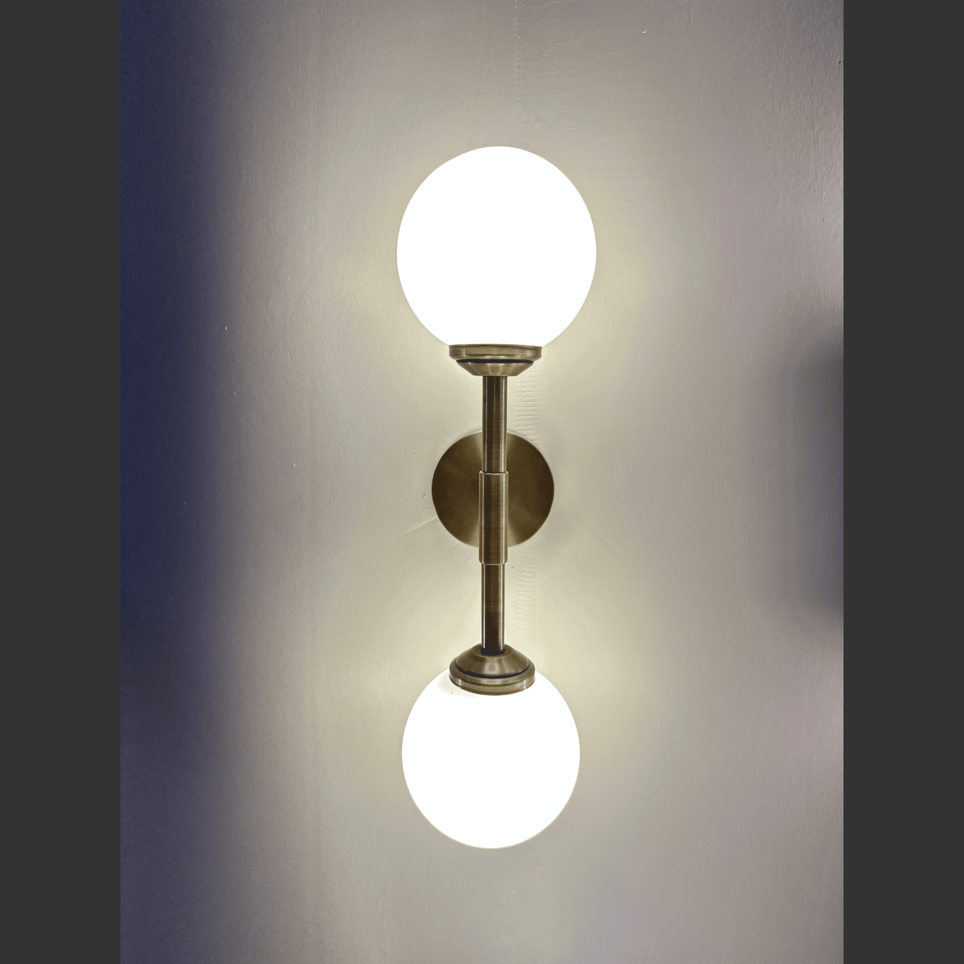Wall-mounted light fixture with two spherical lights on a plain wall.