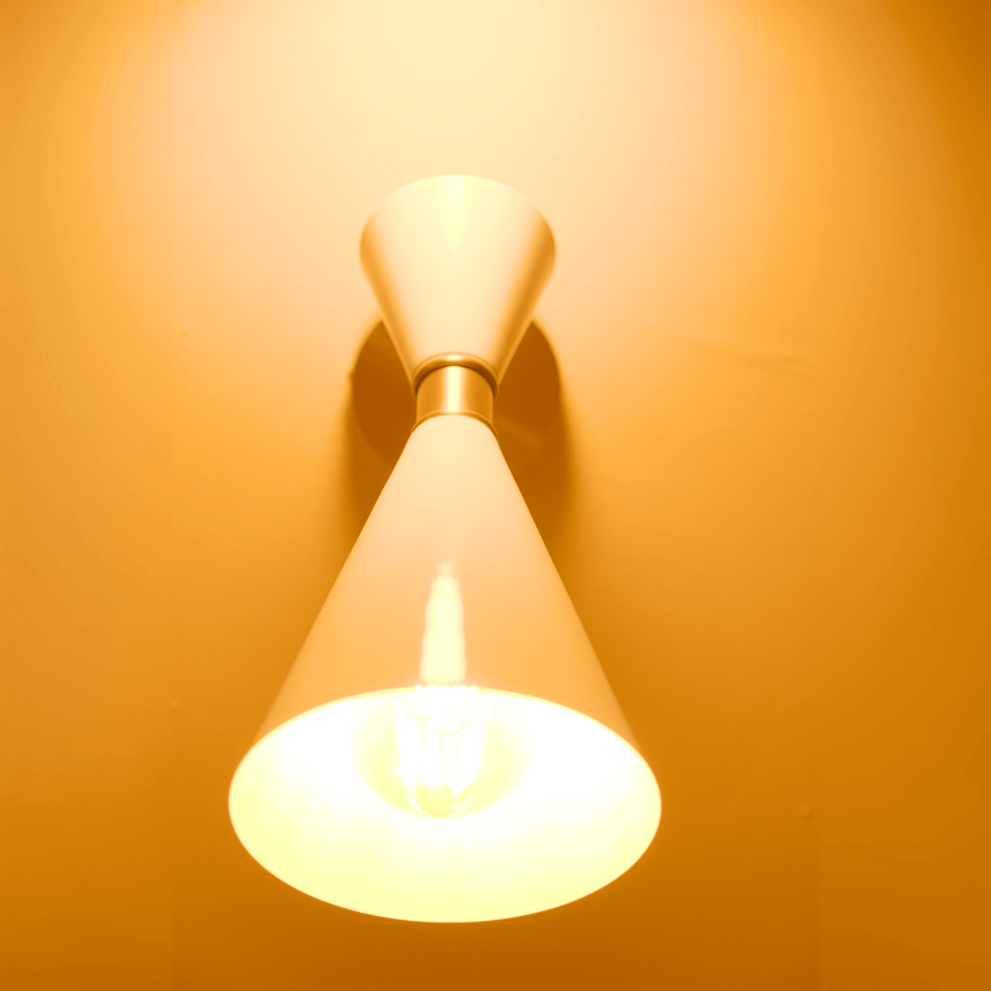Contemporary double-cone white wall sconce with brass accent casting warm light in two directions.