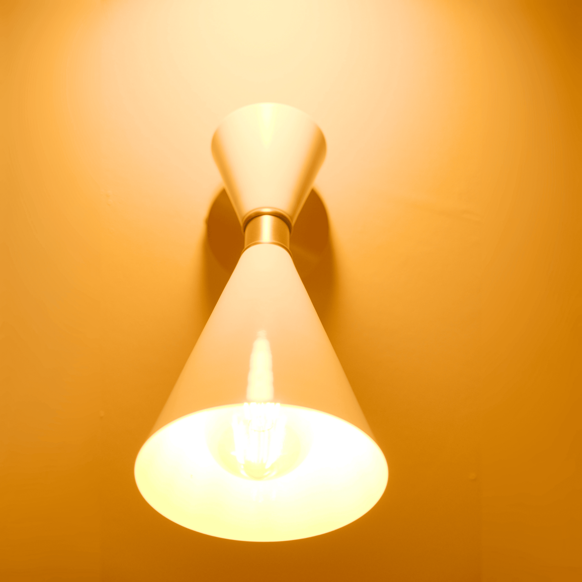 Contemporary double-cone white wall sconce with brass accent casting warm light in two directions.