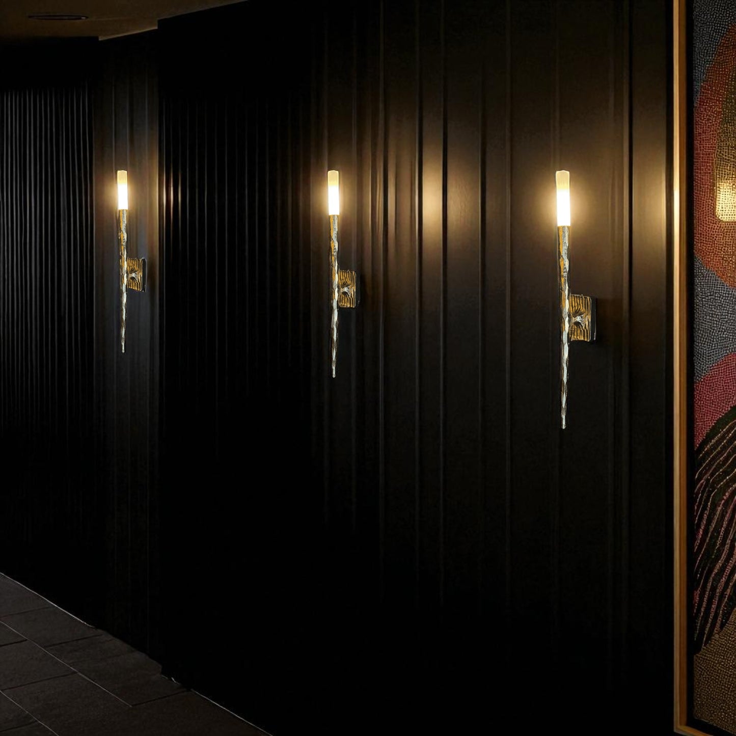 Three modern brass wall sconces illuminate a dark hallway with warm, atmospheric lighting.