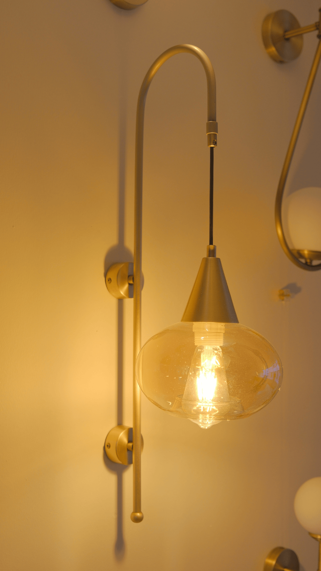Brass wall sconce with curved arm and clear glass bulb, casting warm ambient light.