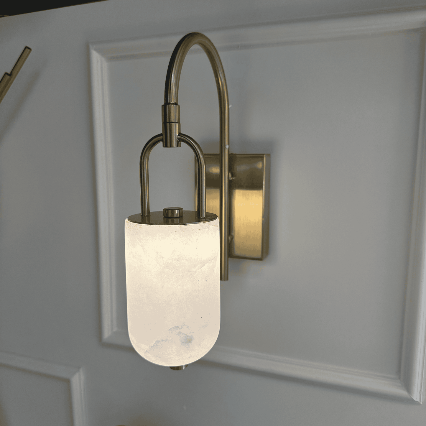 Close-up of curved brass marble wall sconce with glowing alabaster shade.