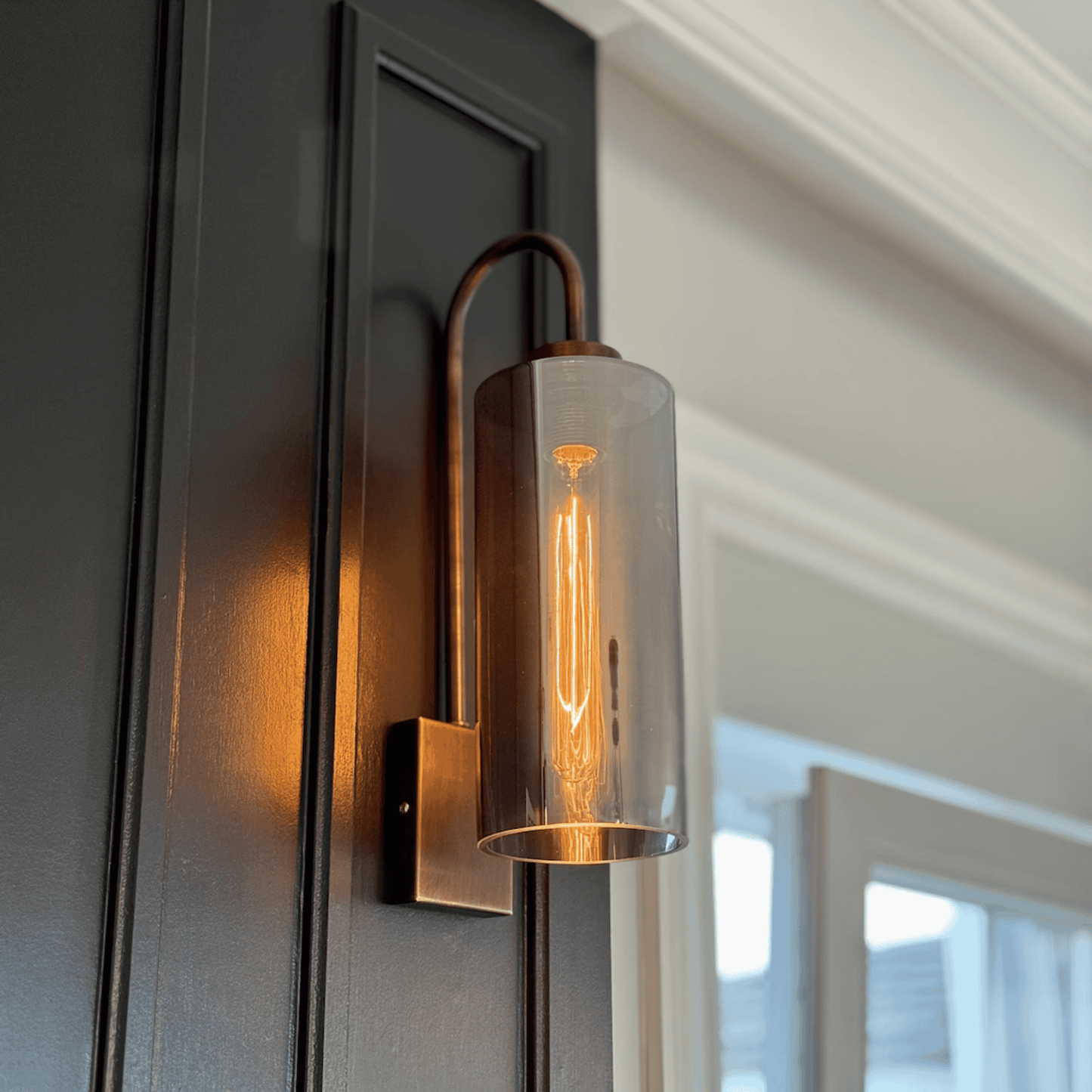 Cylindrical blown glass wall sconce with antique base casting warm ambient light.