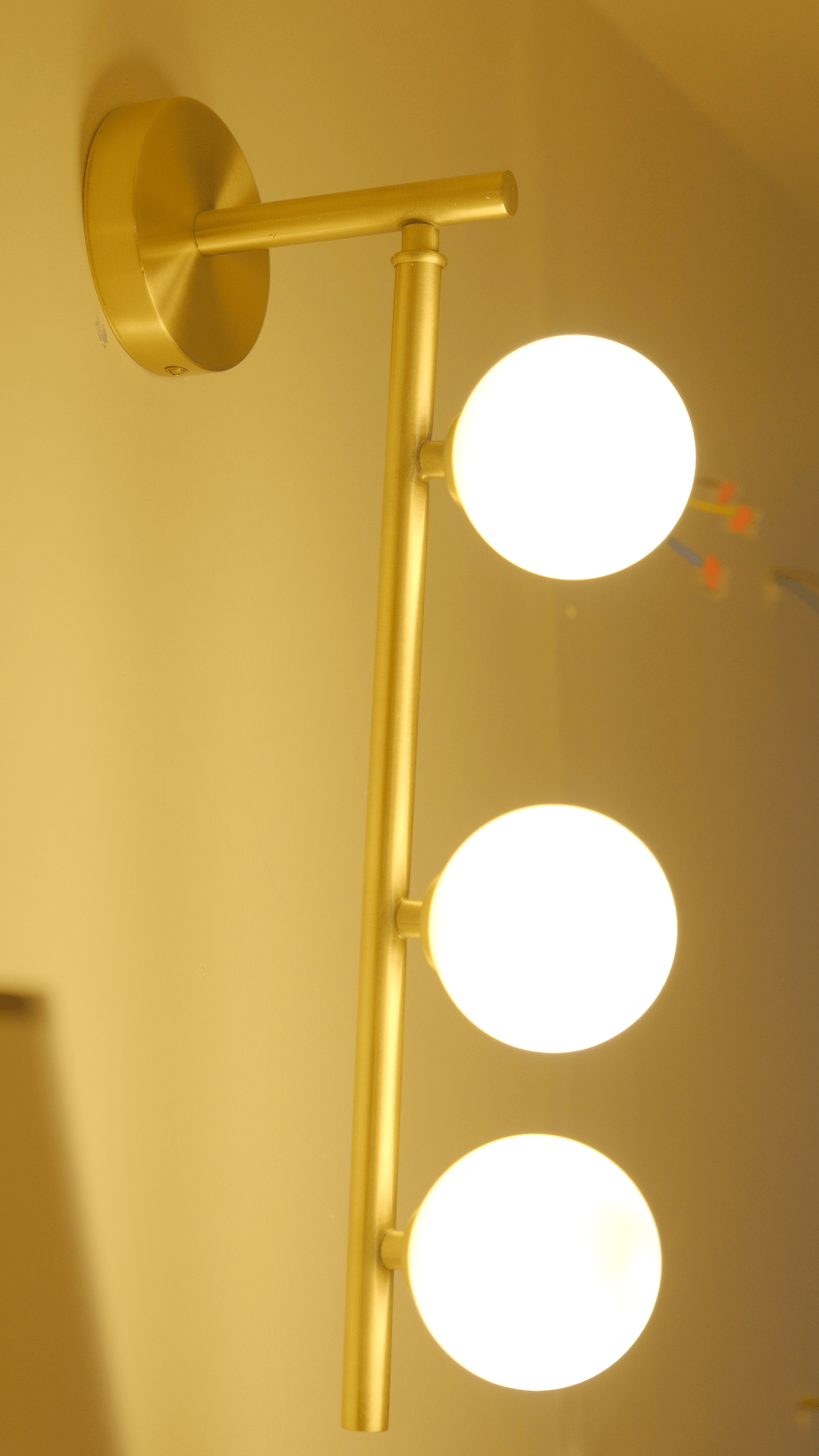 Decorative brass wall sconce with three luminous opal globes in a warm-lit environment.