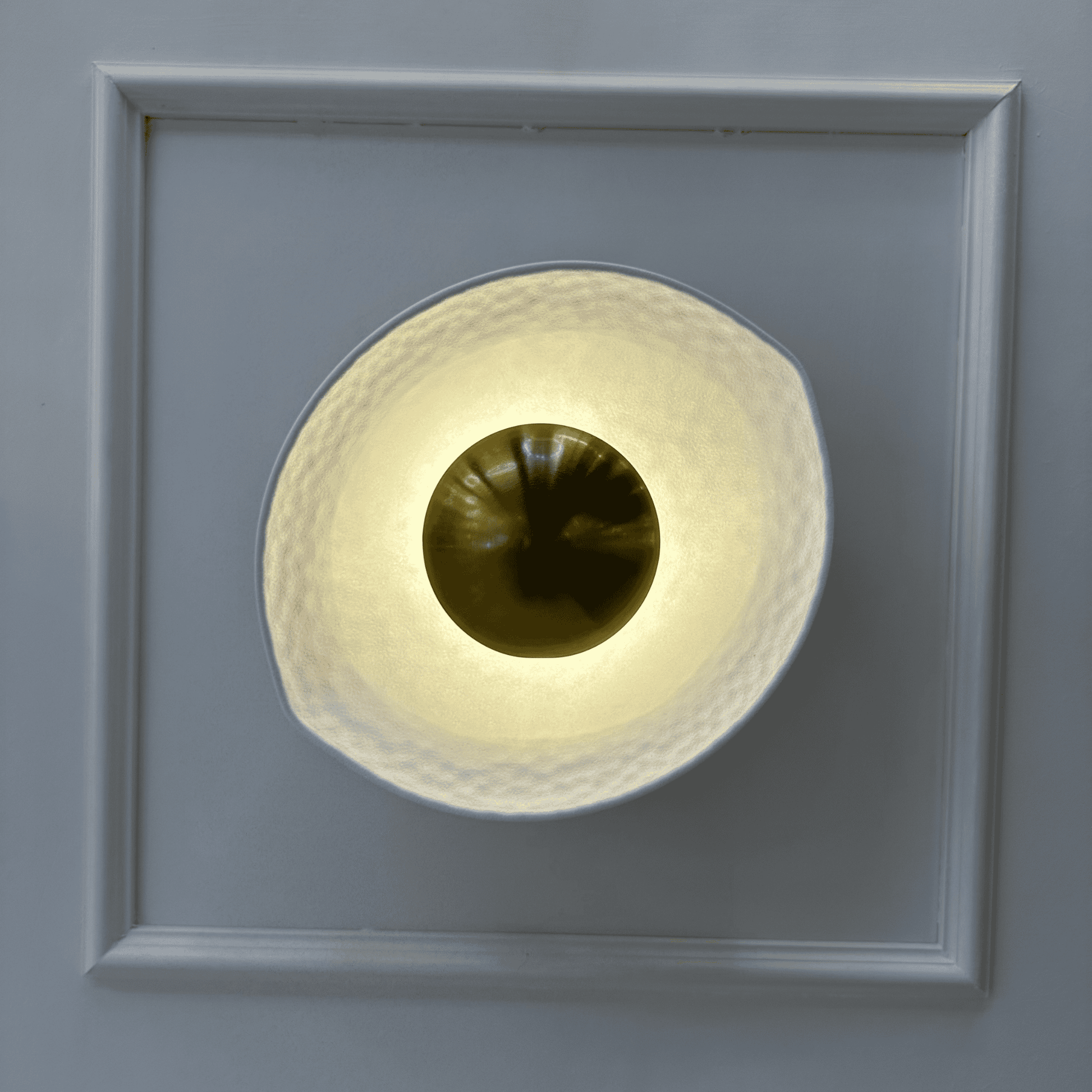 Decorative deco wall sconce with white hammered shade and golden reflective center viewed from the front.