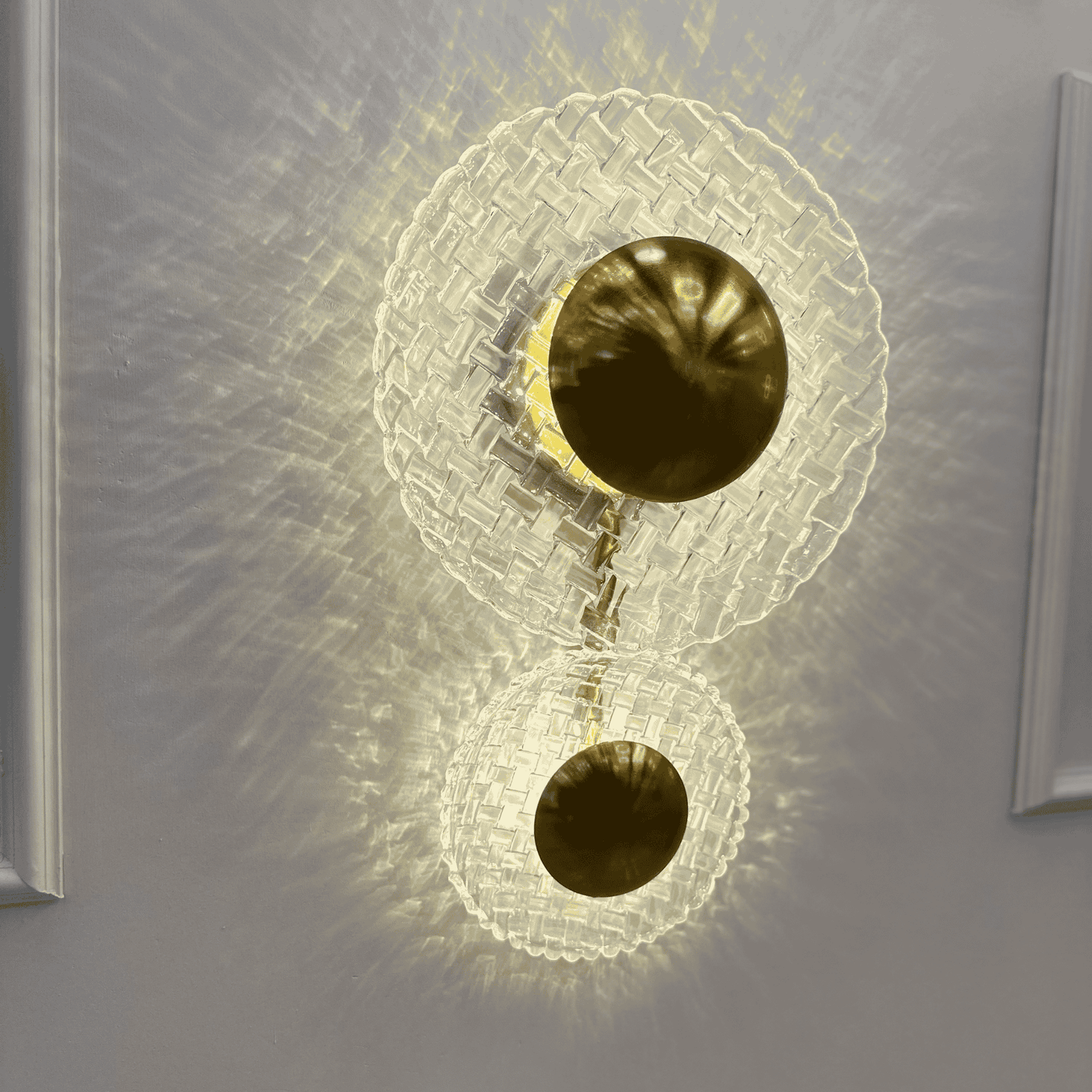 Side view of brass and clear glass wall sconce projecting glowing light pattern on entryway wall.