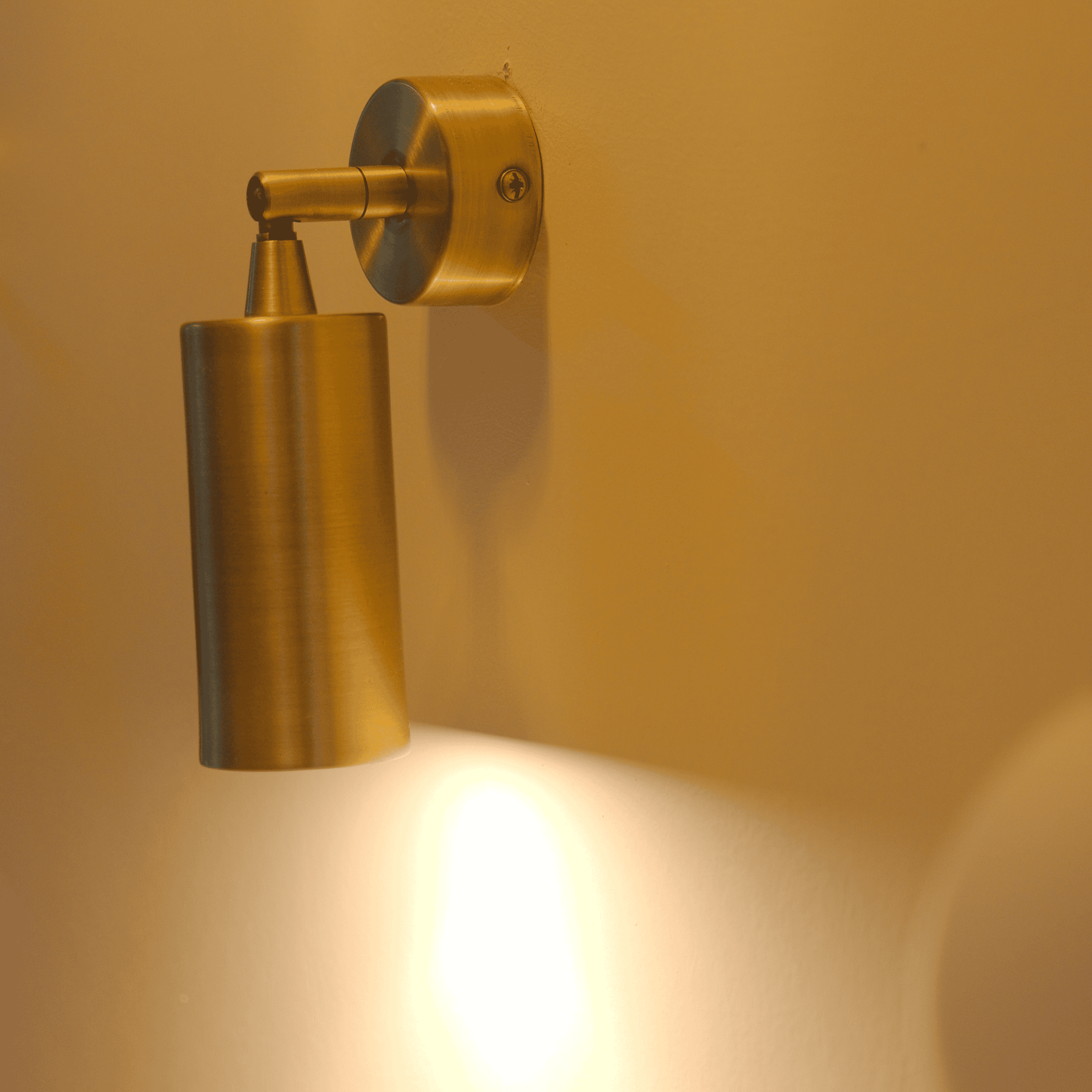 Directional brass cylindrical wall sconce mounted on a wall for adjustable interior lighting.