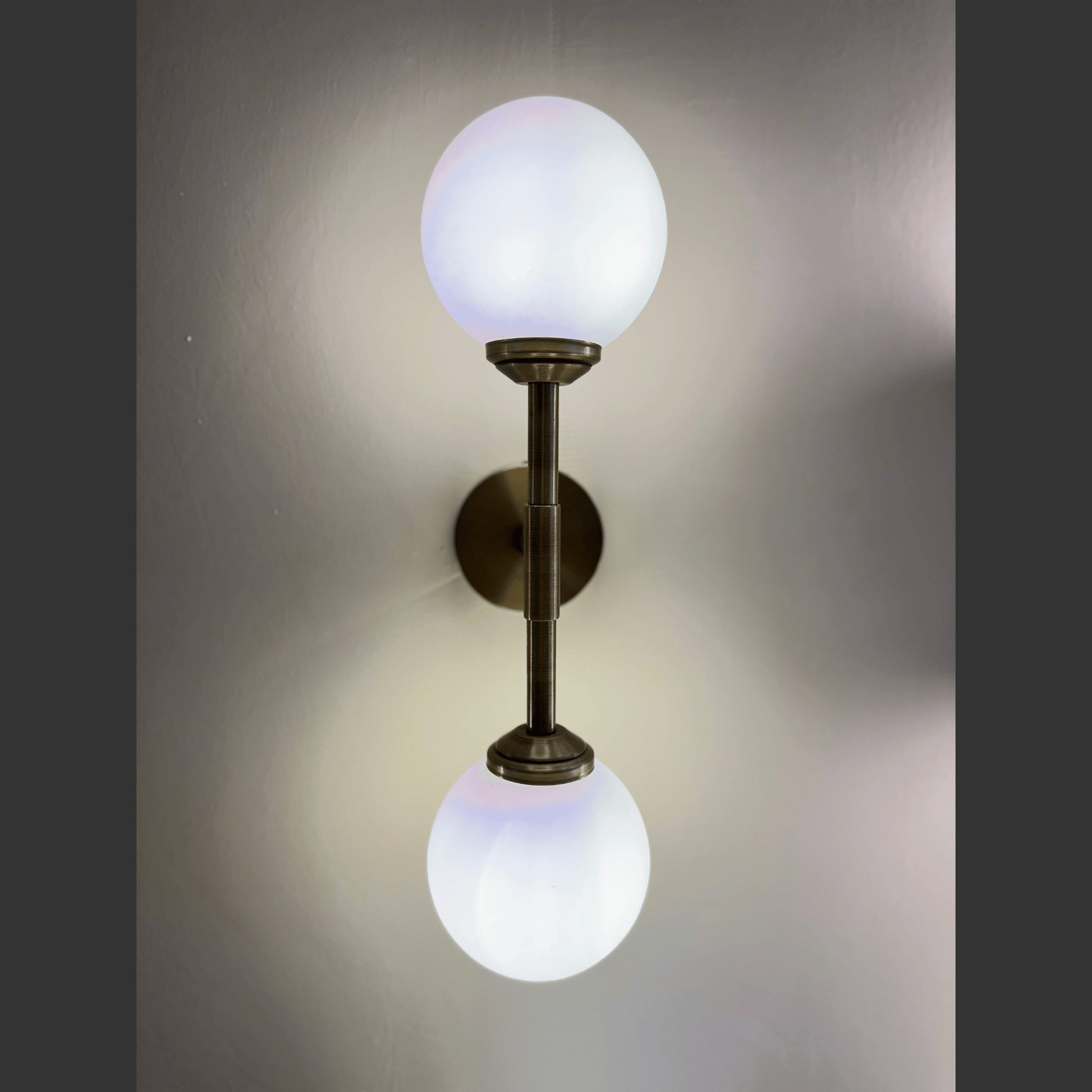 Wall-mounted light fixture with two spherical glass shades on a plain background