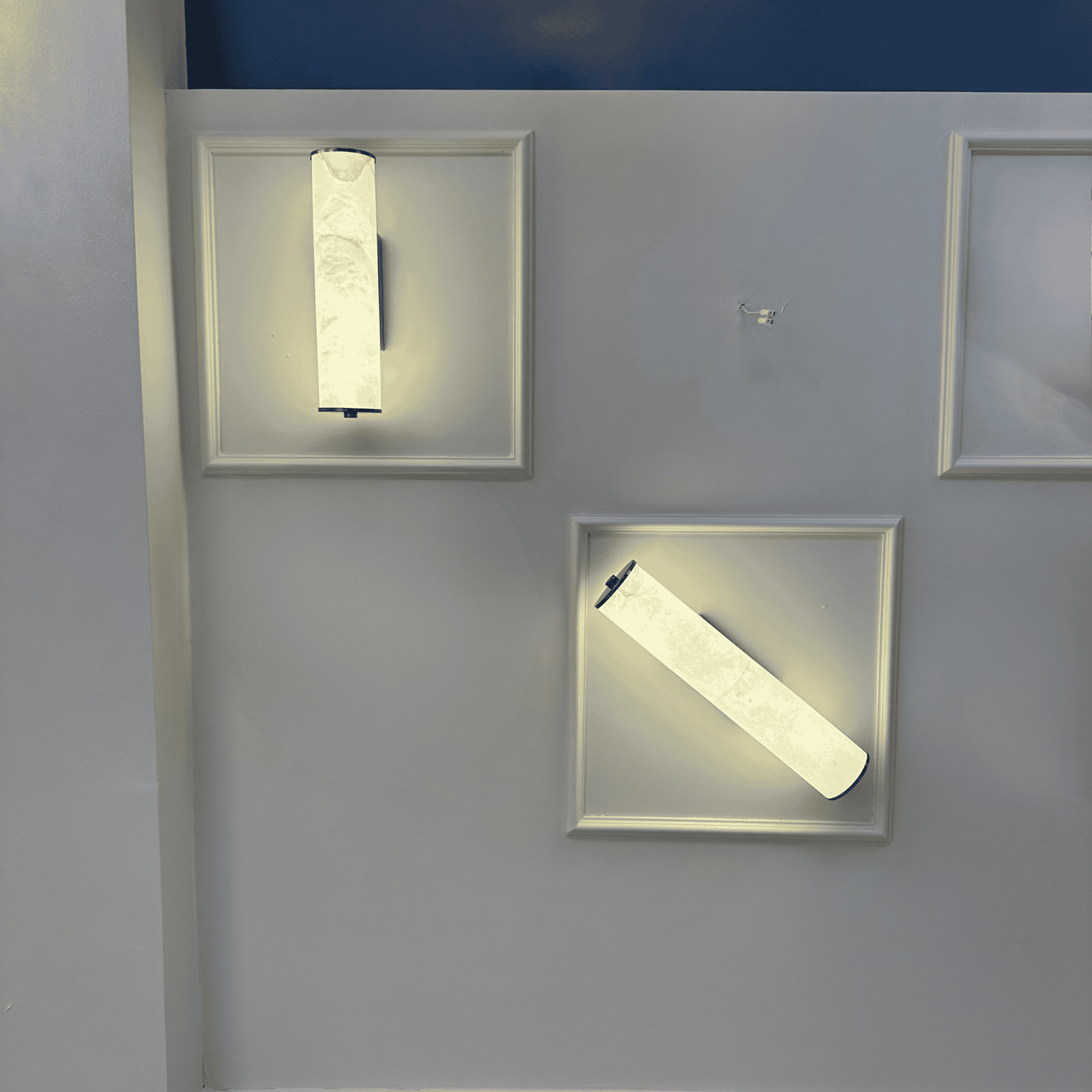 Display of two natural alabaster wall sconces in vertical and angled positions on a gallery wall.