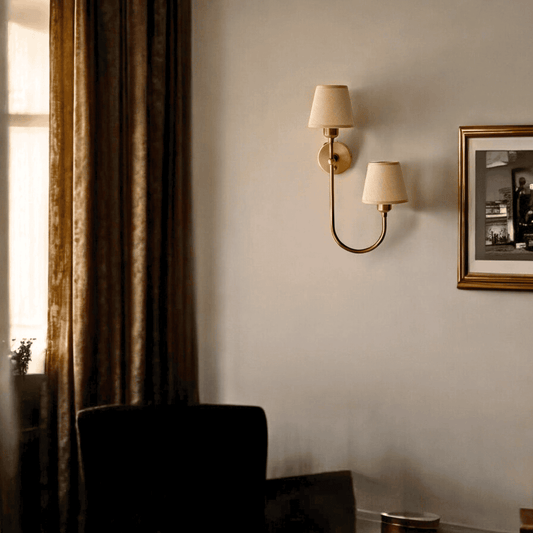 Elegant dual shade fabric wall sconce in aged brass mounted in a cozy living room with warm drapery
