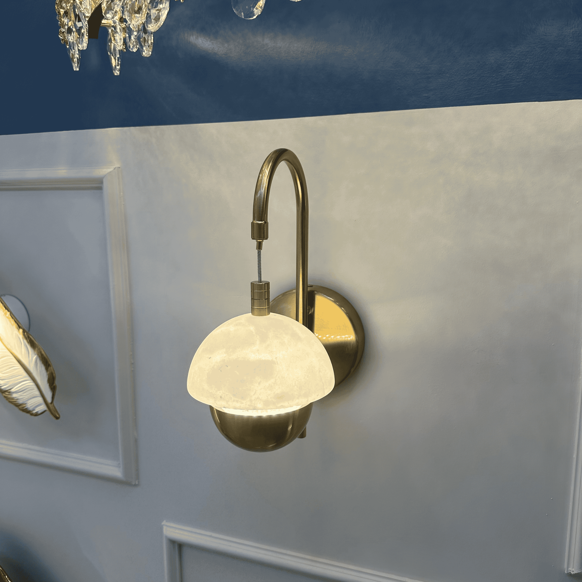 Brass and marble sconce glowing near a chandelier in a luxurious interior.