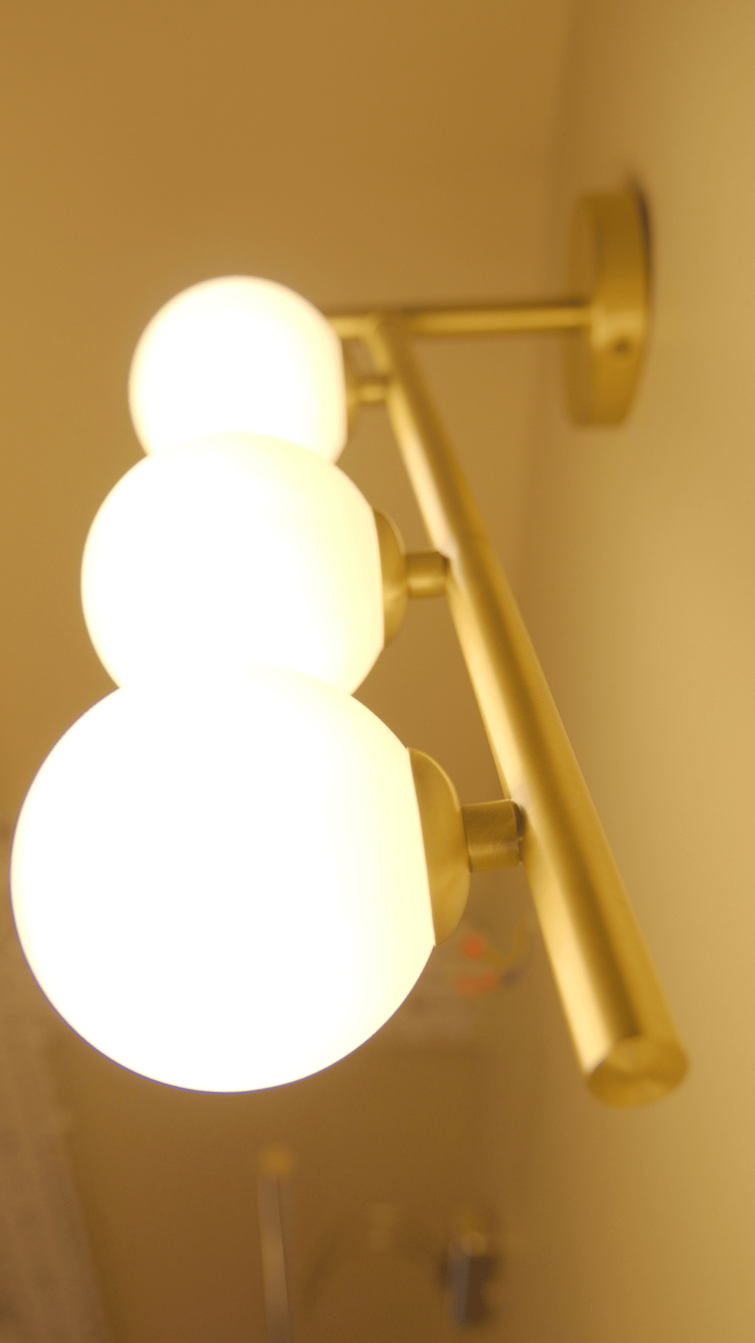 Angled brass wall sconce with three illuminated globes in a warm and elegant lighting setup.