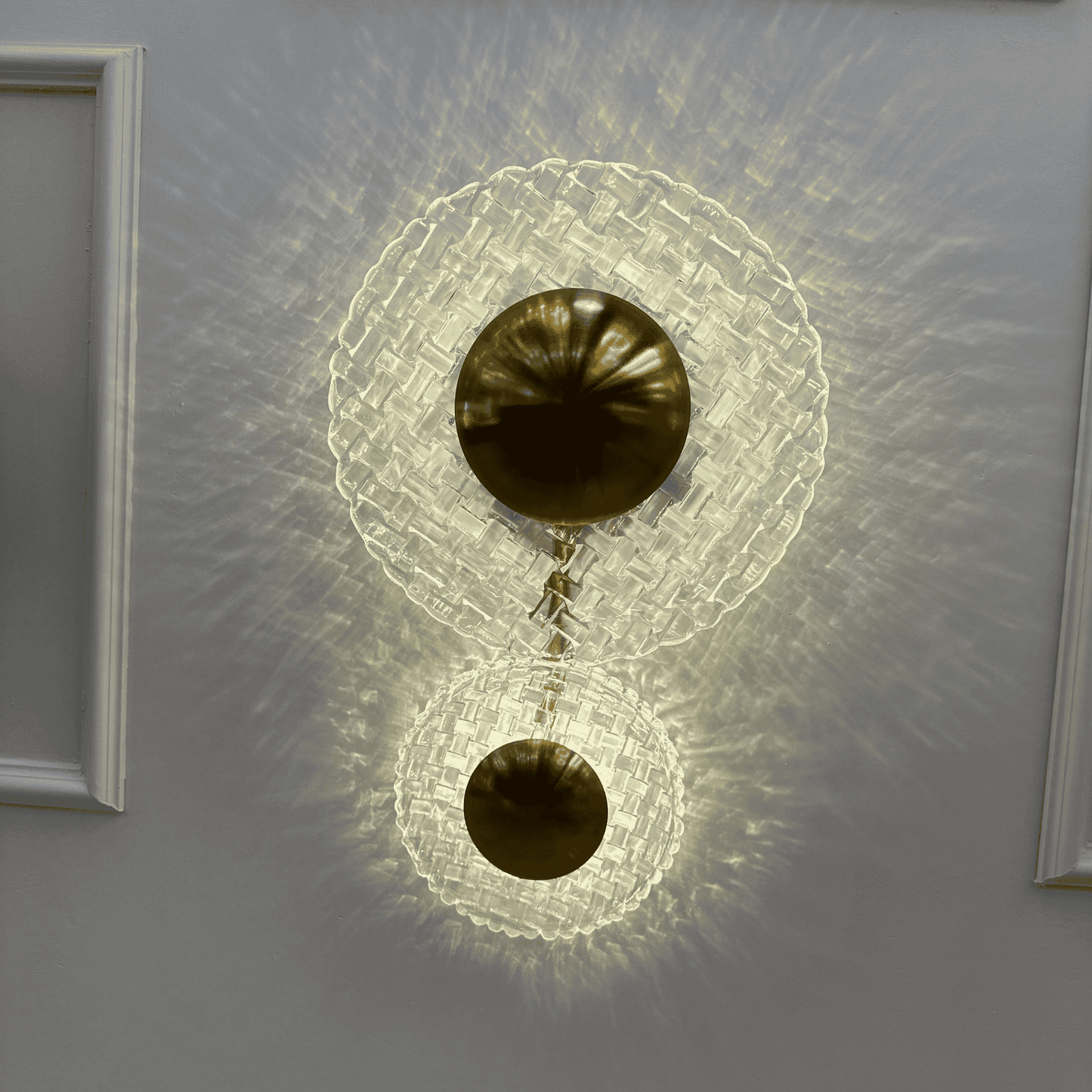 Entryway wall sconce with brass and clear glass design emitting layered, warm lighting.