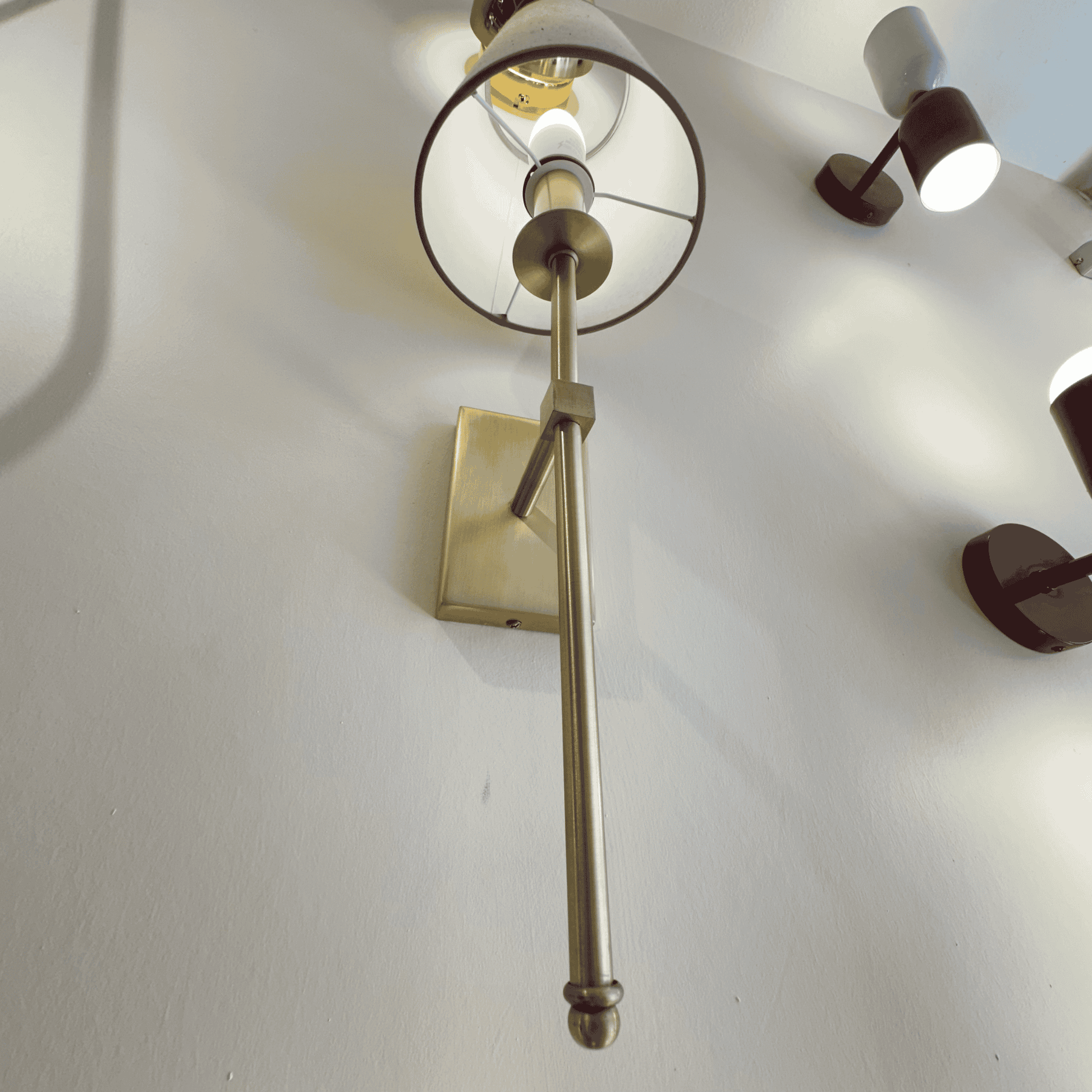 Close-up view of a brass wall sconce showing modern fixture details and fabric shade frame against a white wall.