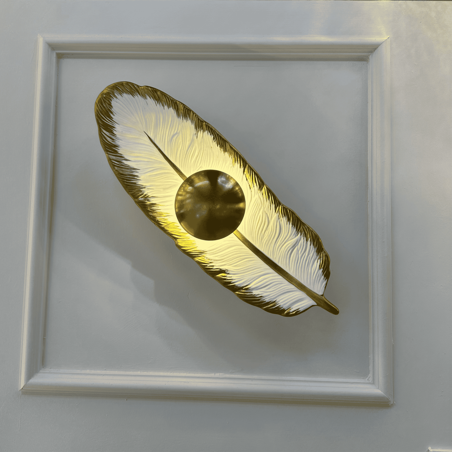 Porcelain feather wall light with a brass LED core glowing against a decorative paneled wall for ambient lighting.