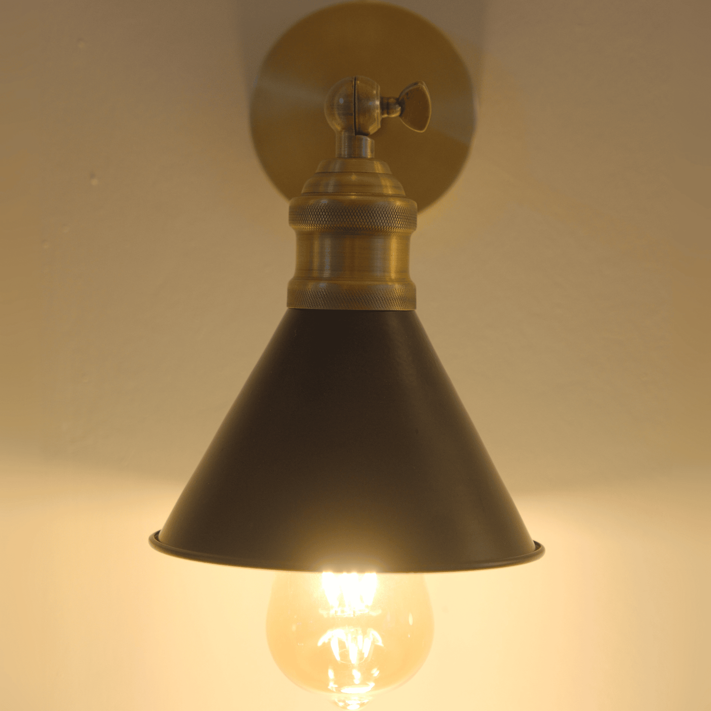Glowing black and brass cone wall sconce viewed from the front.