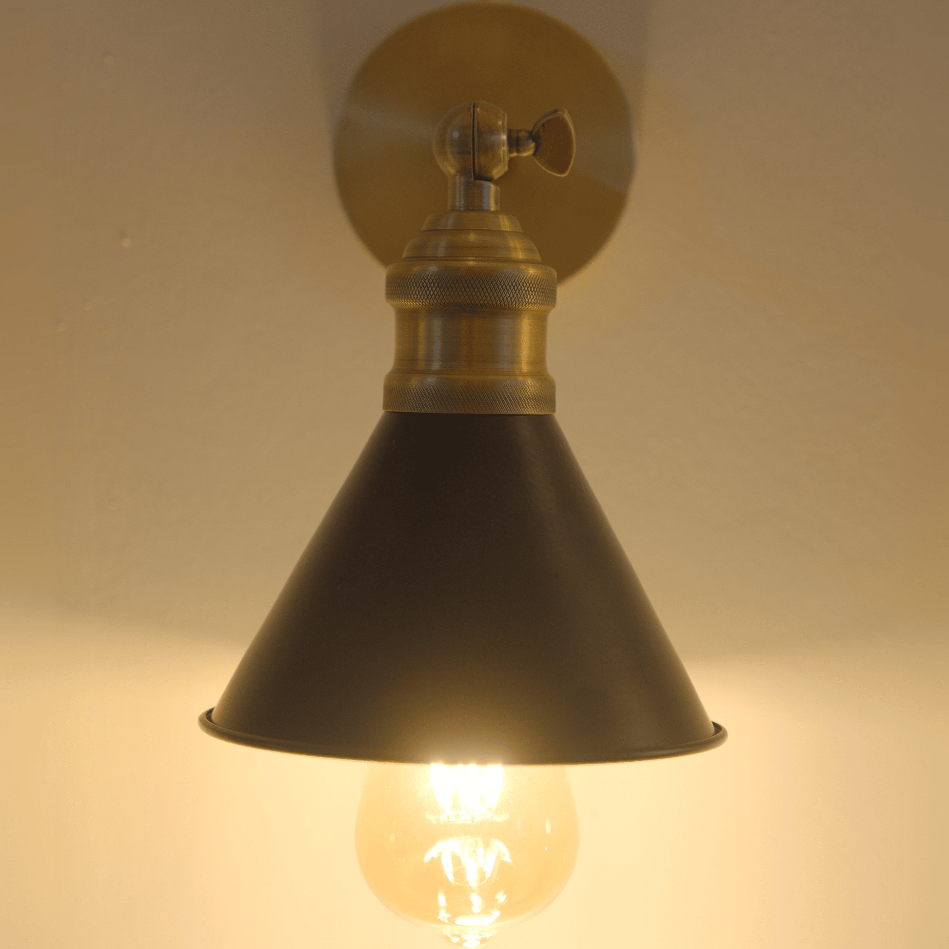 Glowing black and brass cone wall sconce viewed from the front.