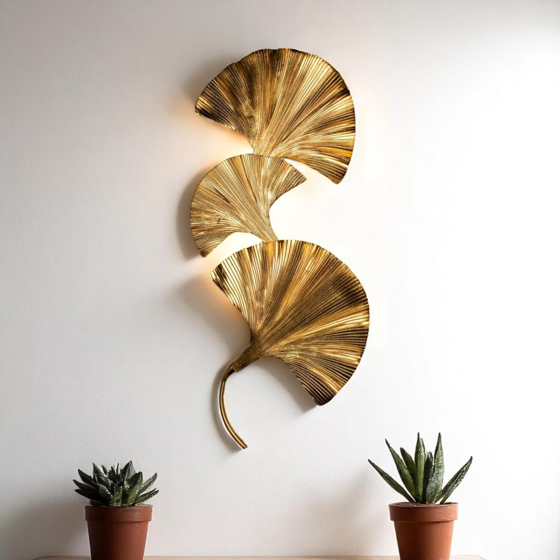 Gold ginkgo leaf wall sconce on a white wall, styled between potted plants