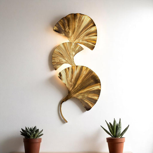Gold ginkgo leaf wall sconce on a white wall, styled between potted plants