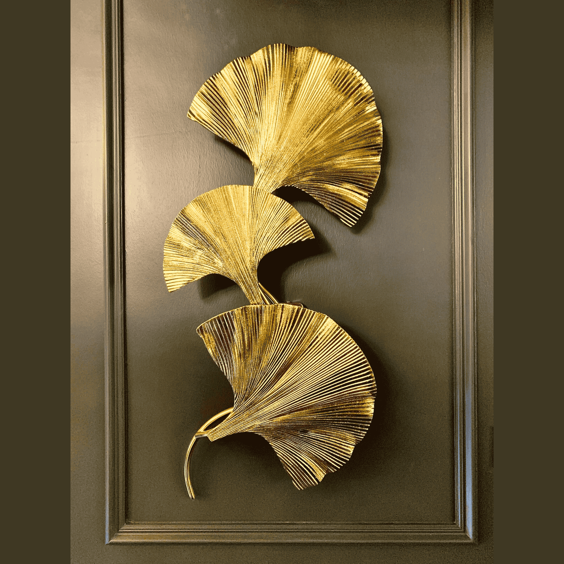 Triple ginkgo leaf brass wall sconce with soft LED glow on a warm textured wall