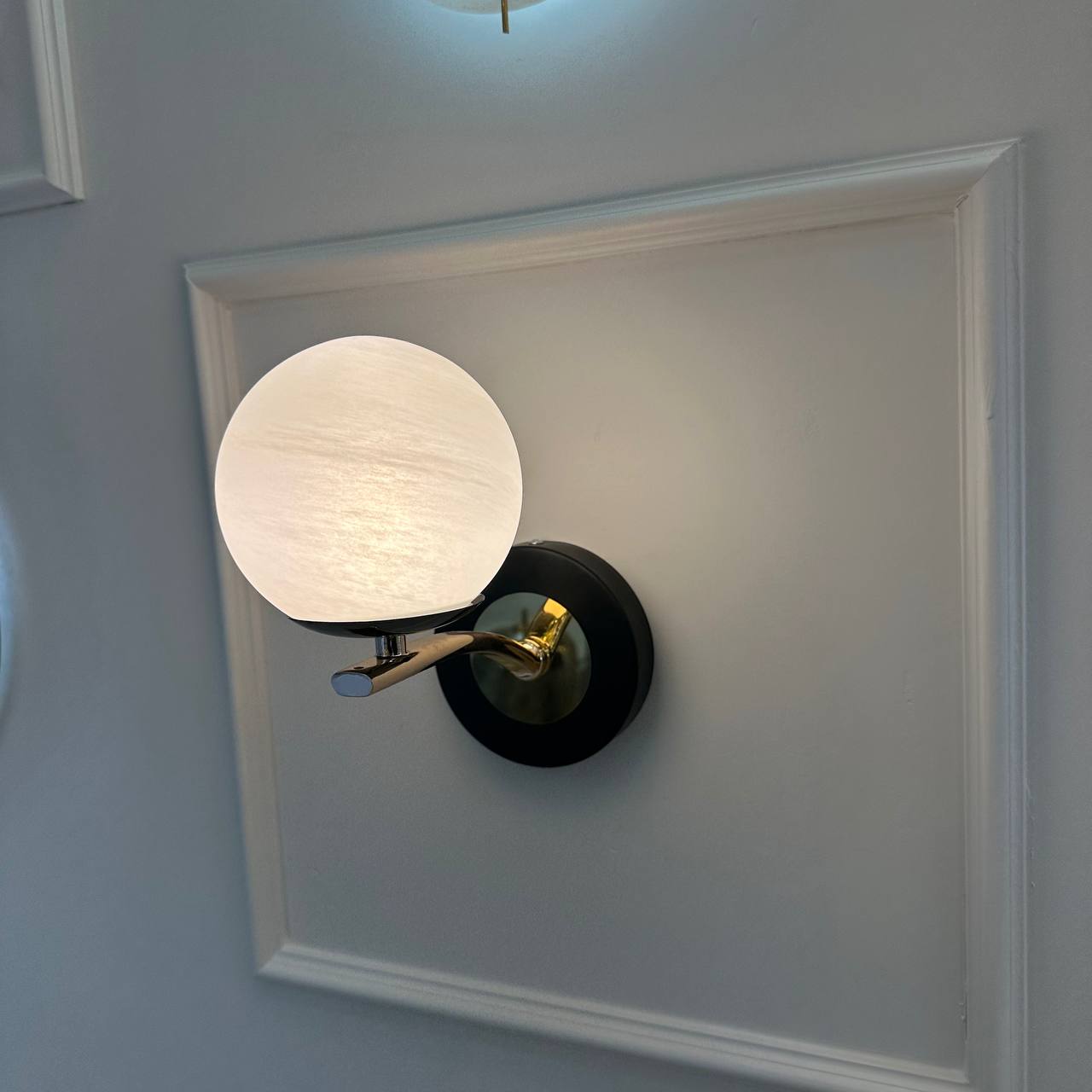 Globe-style alabaster sconce with brass and black elements mounted on a framed wall panel.