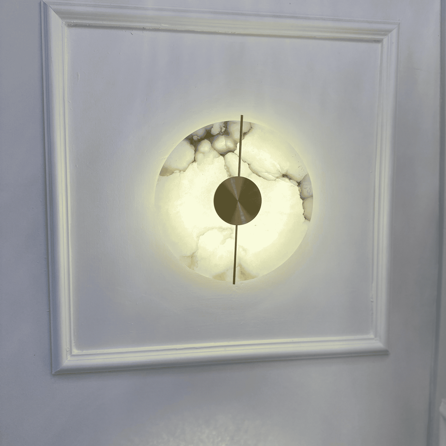 Illuminated marble sconce installed on a paneled white wall.