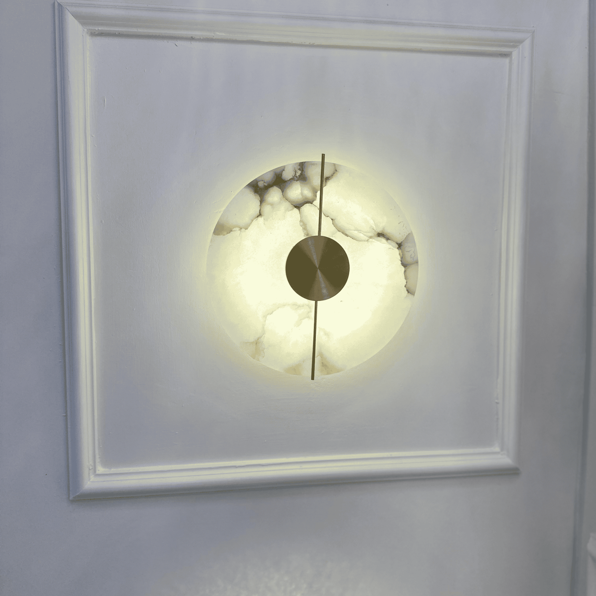 Illuminated marble sconce installed on a paneled white wall.