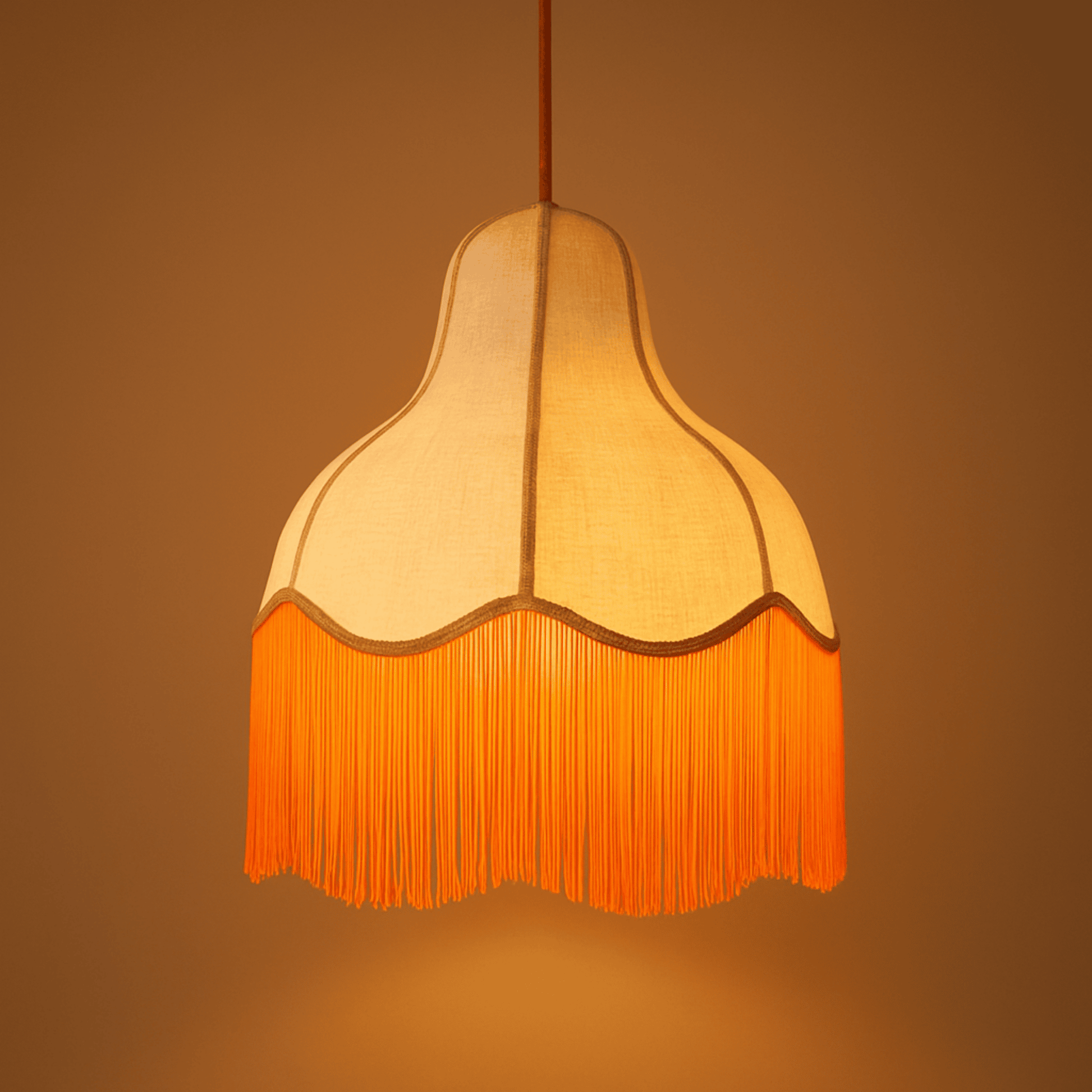 Illuminated pendant light with a curved linen shade and orange fringe, providing warm ambient ceiling lighting.