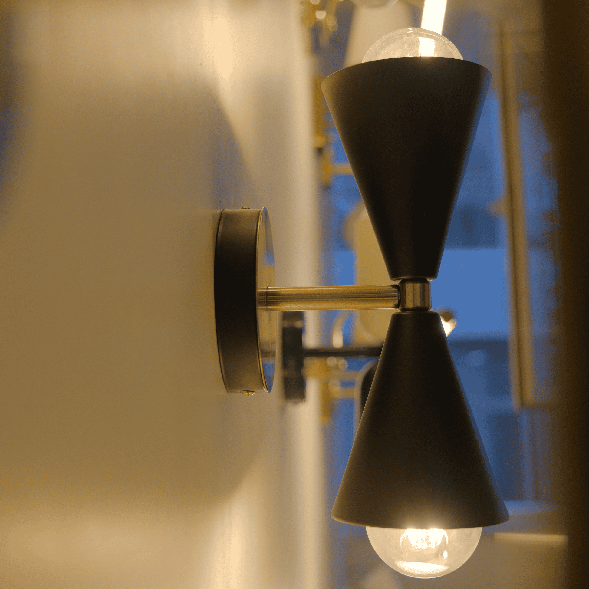 Wall-mounted black cone sconces with brass arms glowing warmly in a modern hallway setting.