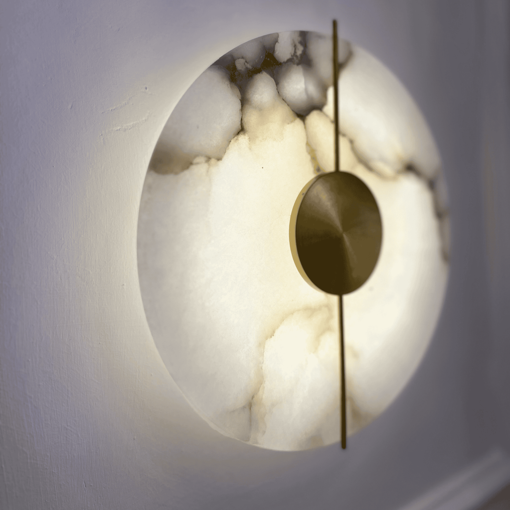 Side angle of a glowing marble sconce with brass center on a wall.