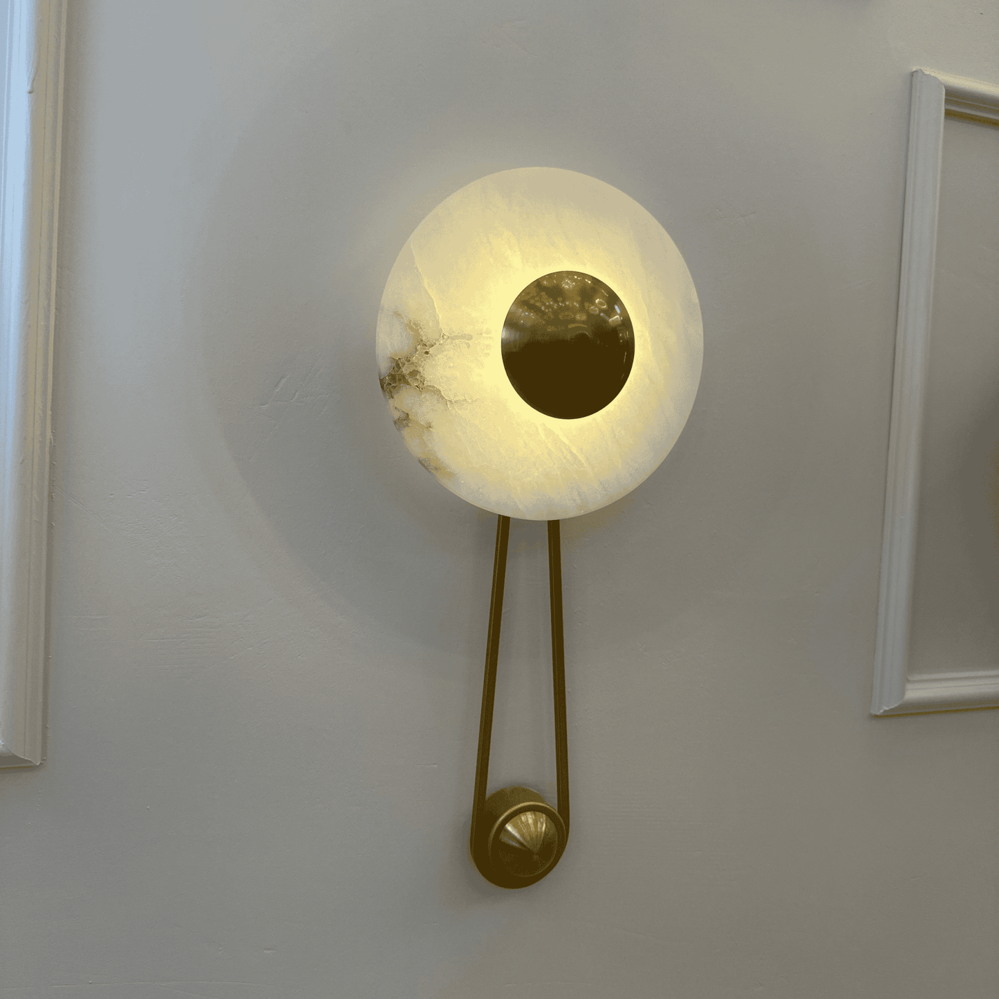 Softly lit alabaster wall light with a central round brass disc mounted on a pale wall.