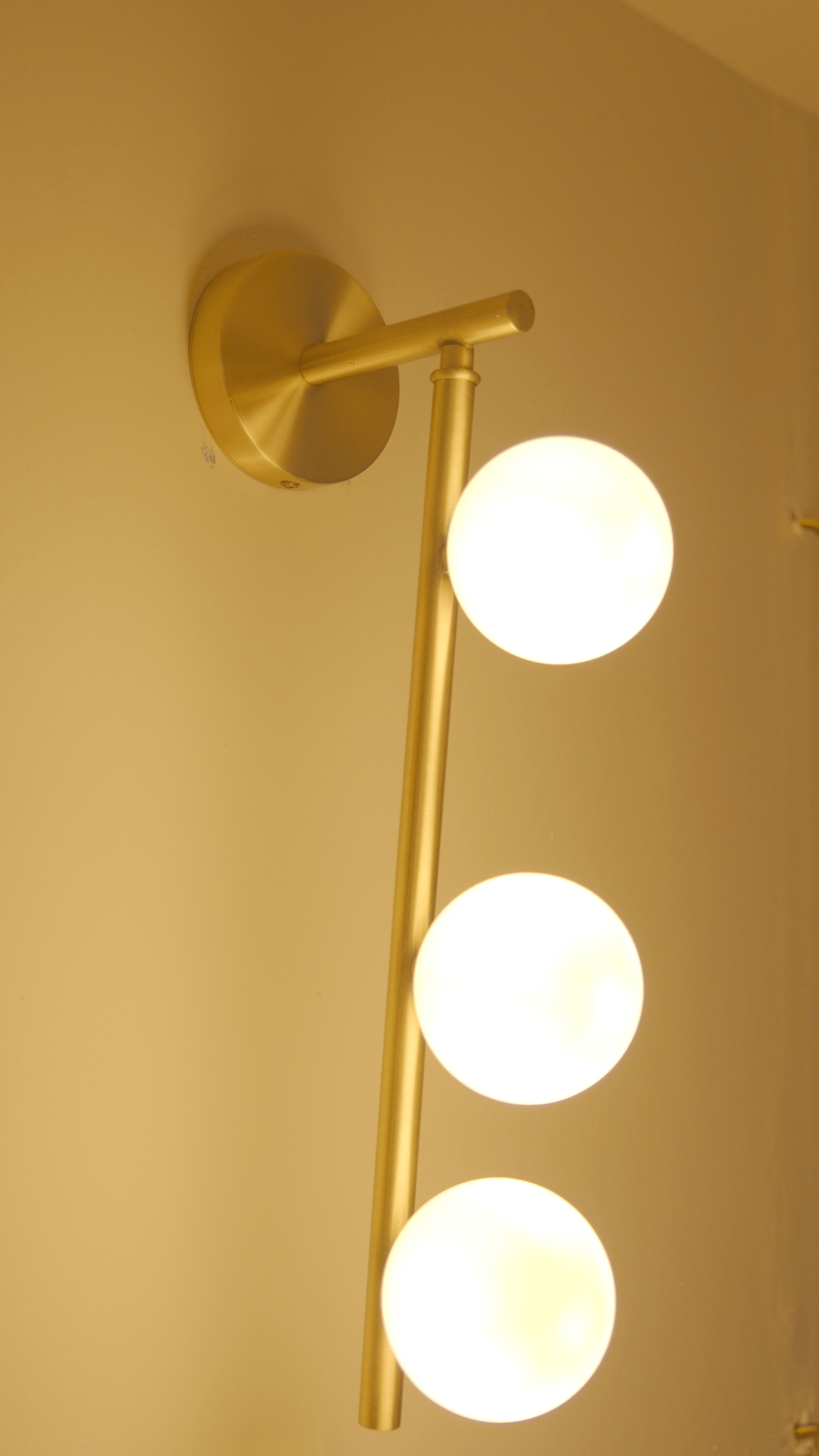 Warmly lit brass wall sconce with three frosted globes for ambient room lighting.