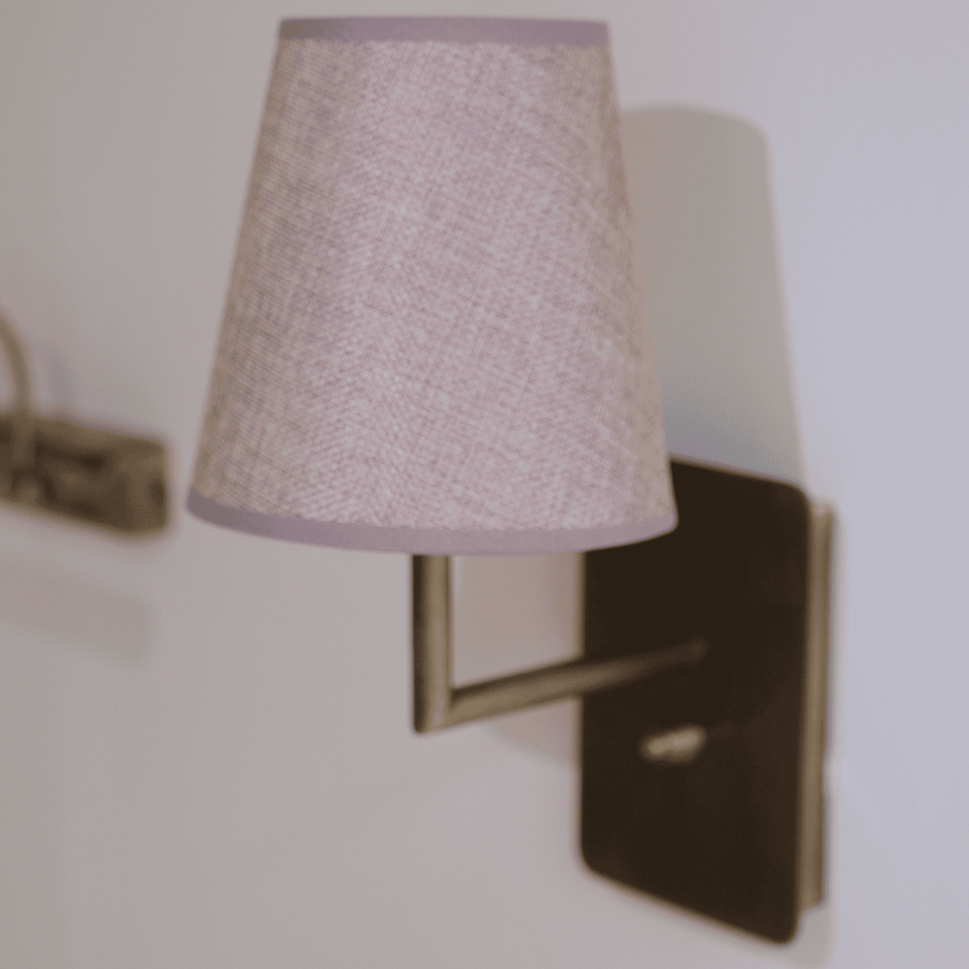 Lavender fabric wall sconce on brushed metal base providing soft ambient glow.