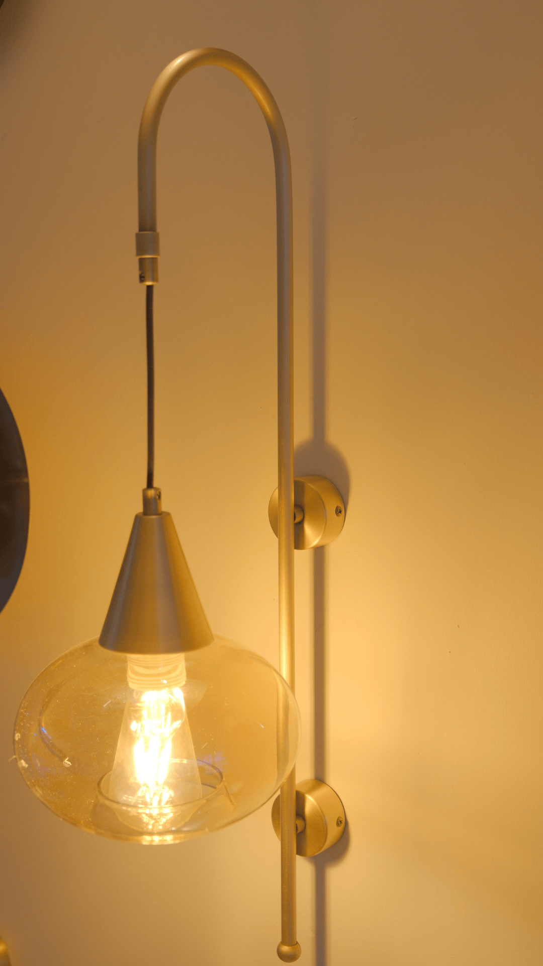 Long-arm brass sconce with clear glass shade and exposed LED bulb.