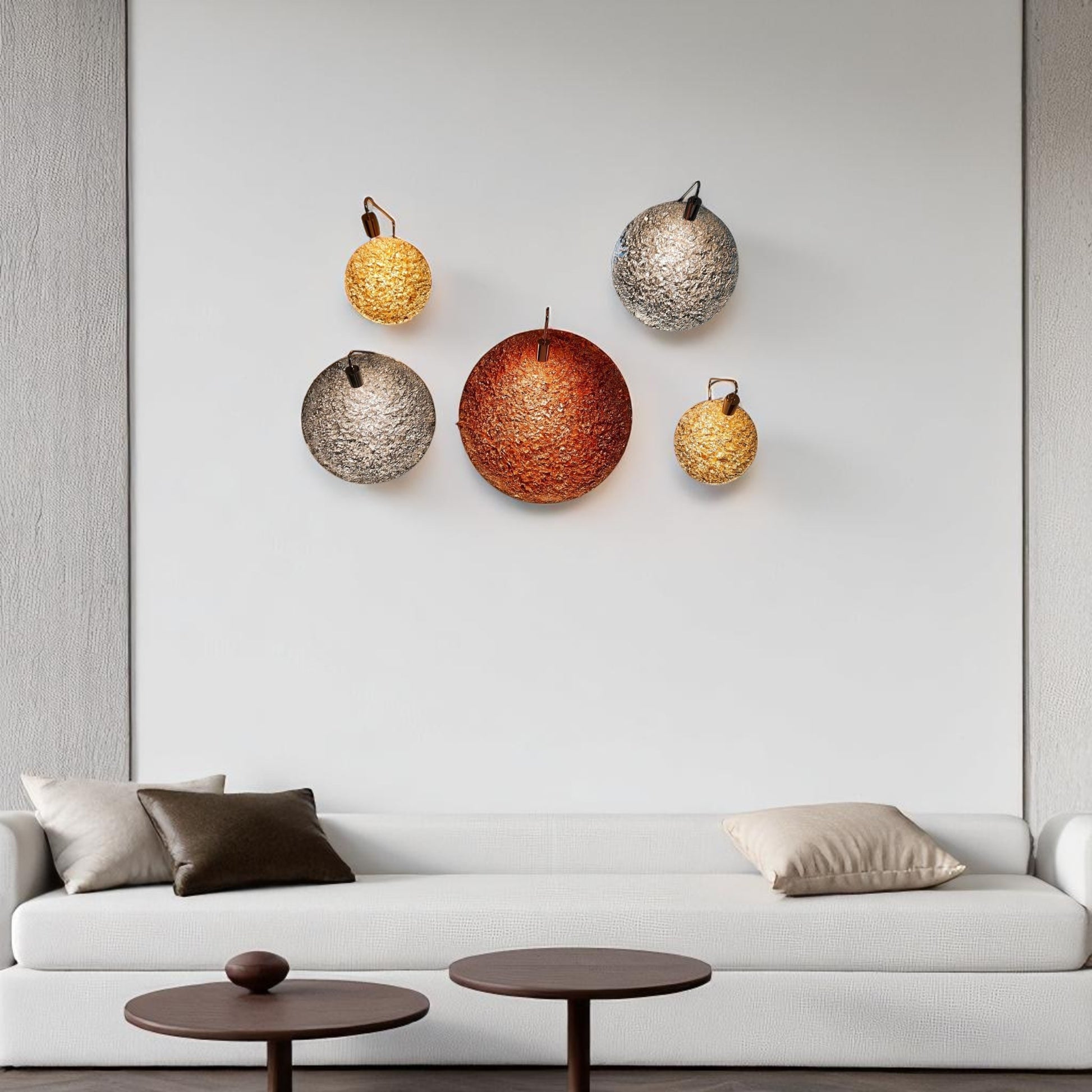 A set of five round textured brass wall sconces in gold, silver, and copper finishes mounted above a white sofa in a modern living room
