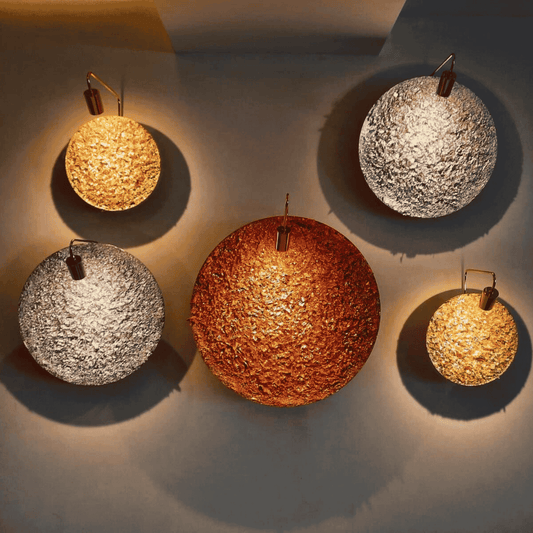 Sculptural brass wall sconce with a textured circular face, glowing softly on a dark interior wall