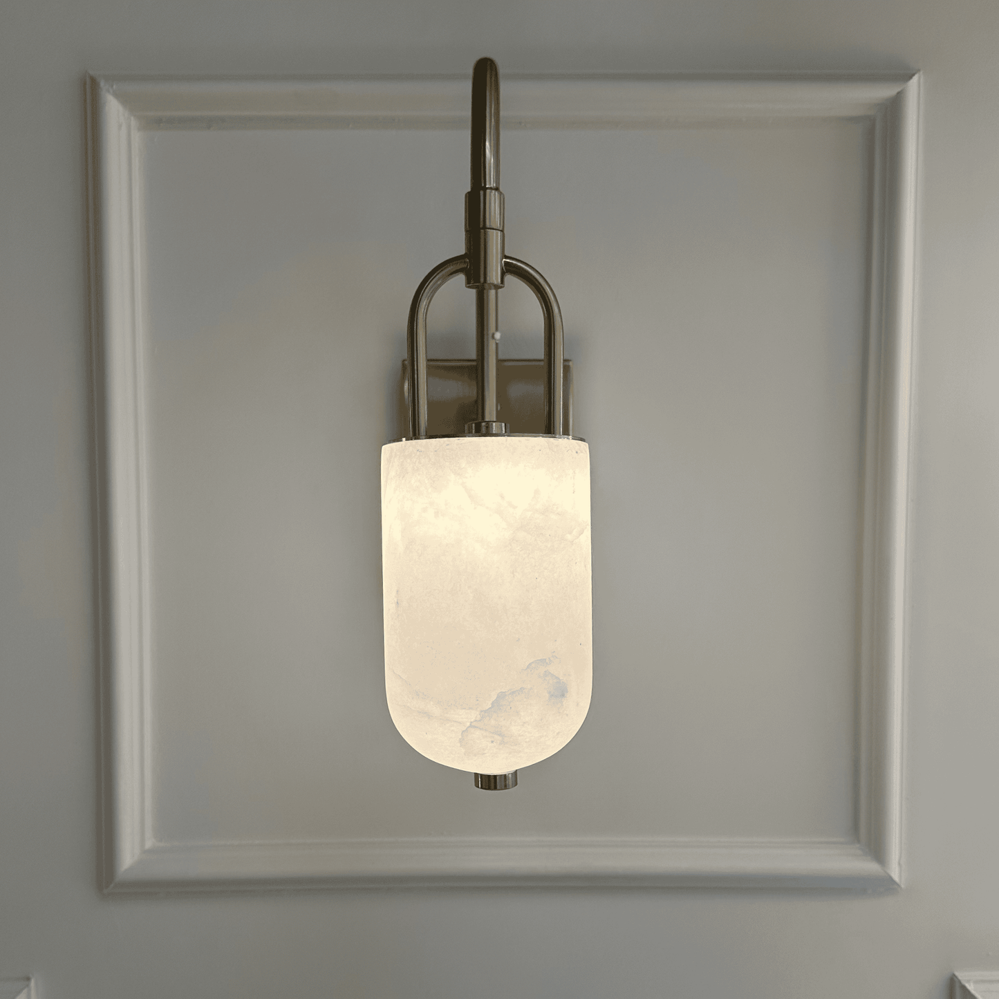 Arched brass and alabaster marble wall sconce emitting soft white glow.