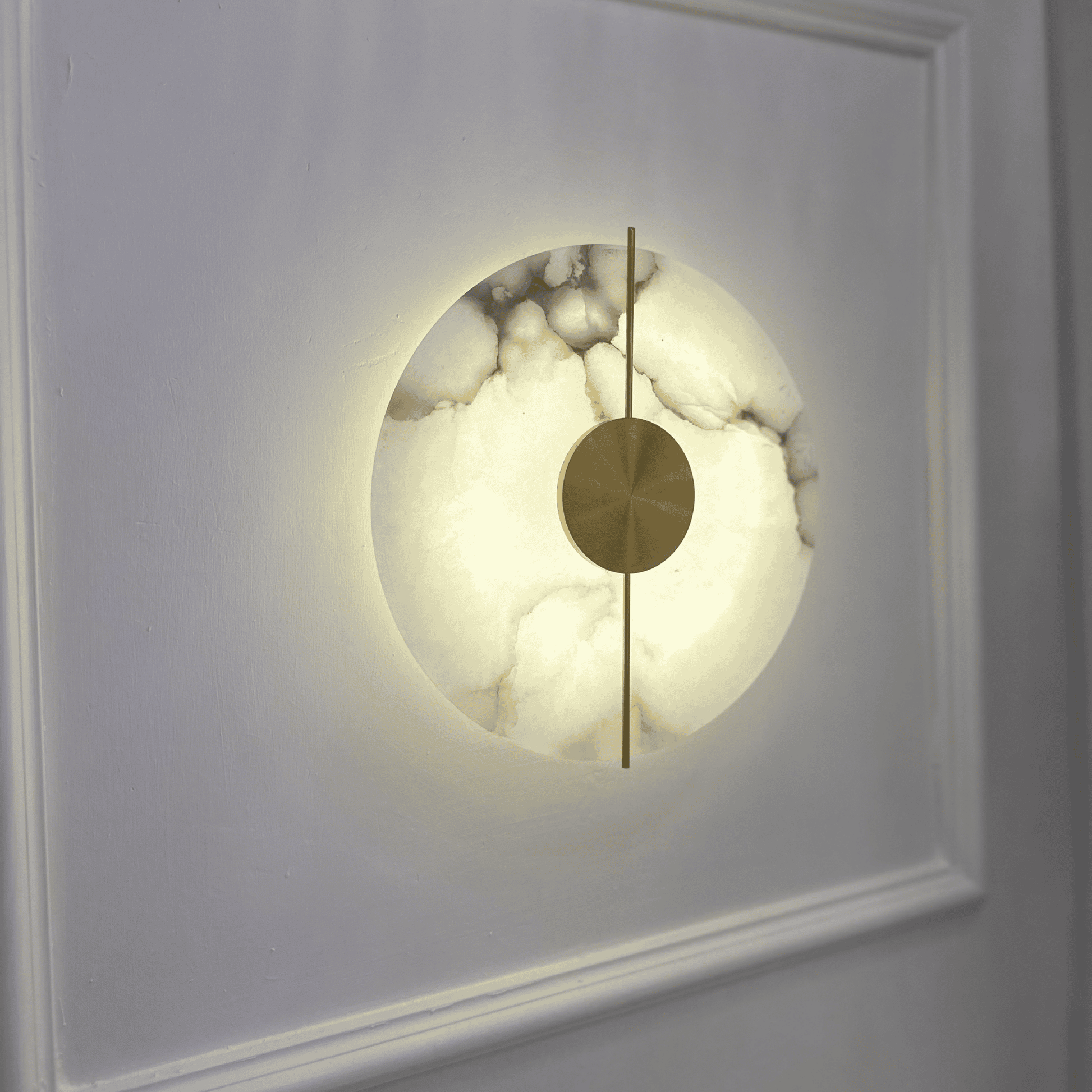 Marble sconce with central brass detailing and soft backlight on a white wall.
