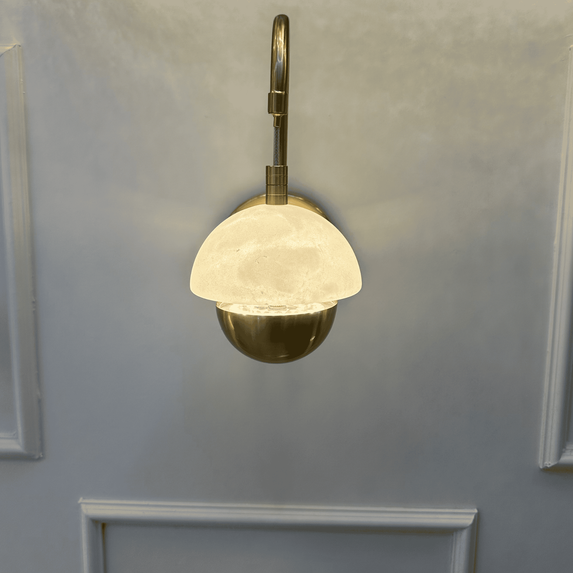 Modern marble sconce with brass fixture and dome-shaped shade mounted on a paneled wall.