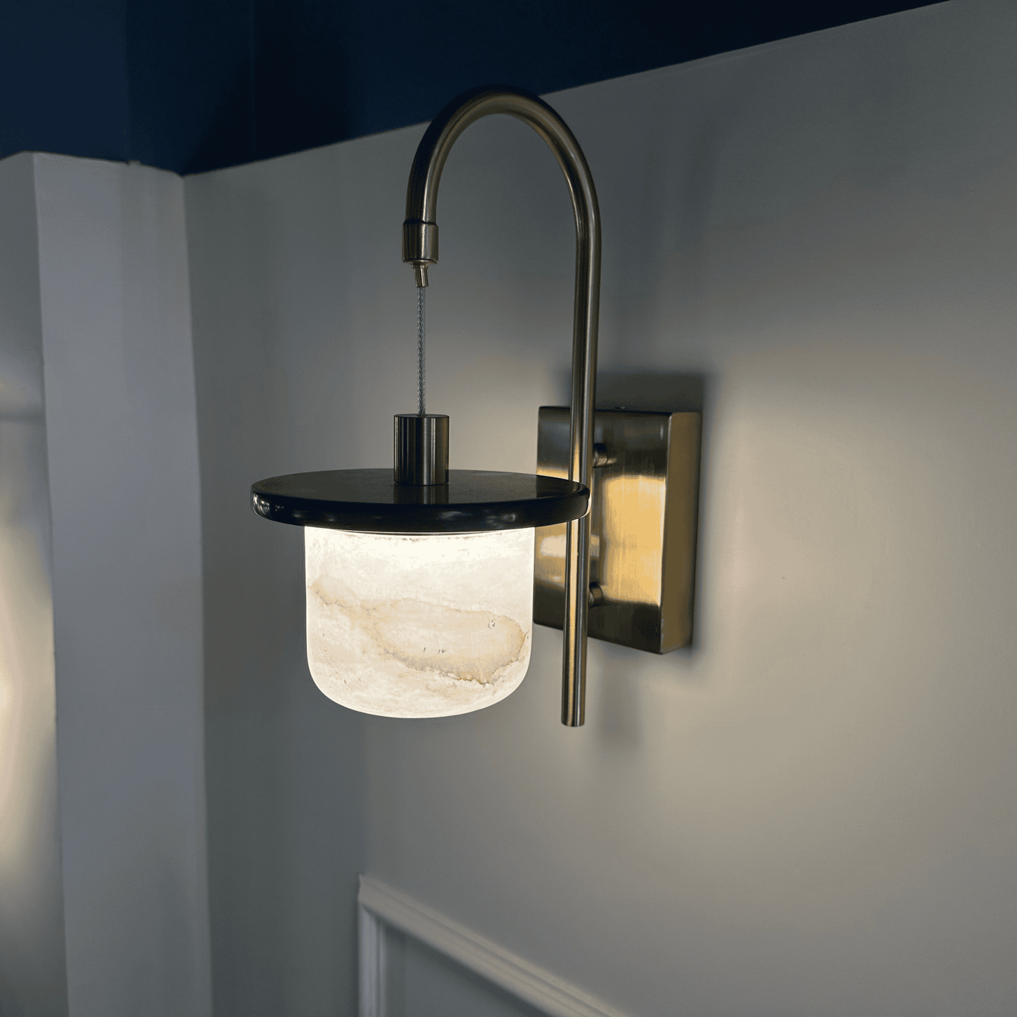 Marble sconce wall light with brass arm and alabaster shade on neutral wall.