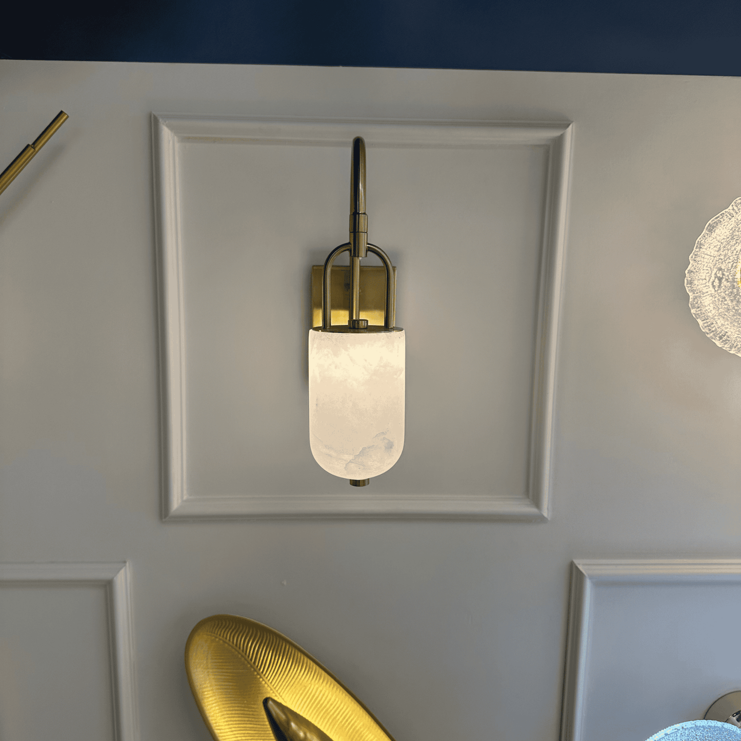 Brass arched marble wall sconce with soft ambient light on white panel wall.