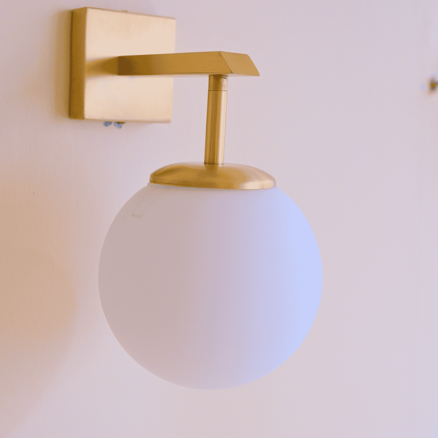 Matte white globe sconce with brass arm mounted on a neutral wall for clean modern lighting.