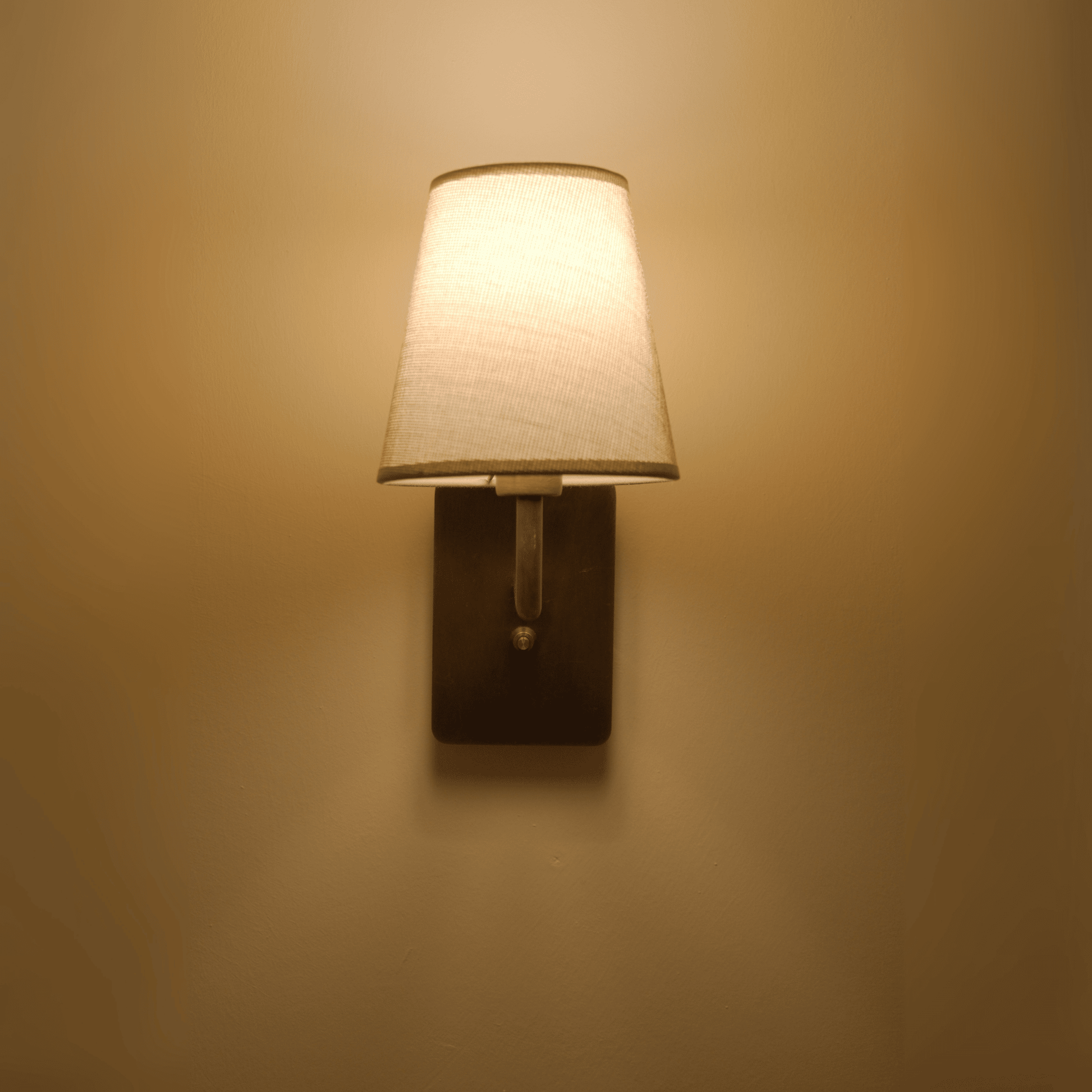 Minimalist bronze wall sconce with tapered shade providing soft lighting.